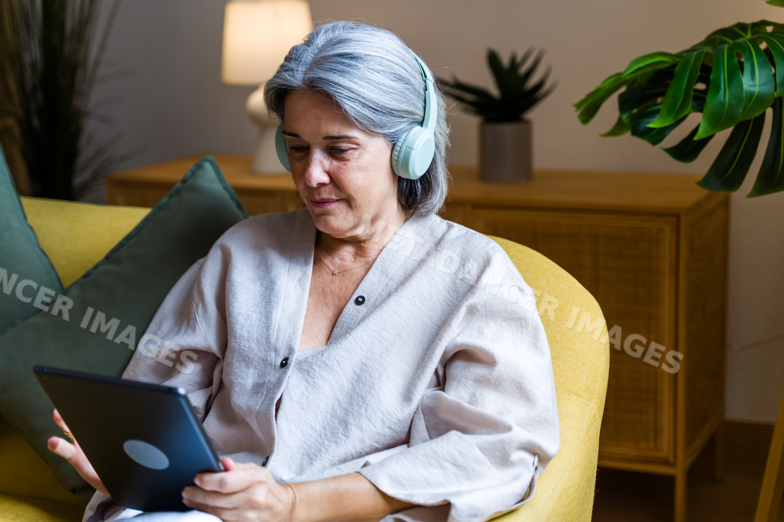 White woman wearing headphones using tablet in living room