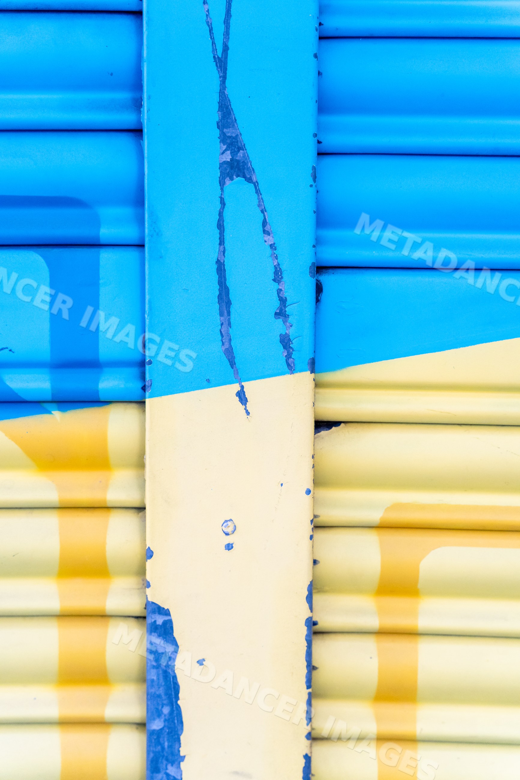 Weathered metal shutter with peeling blue and yellow paint