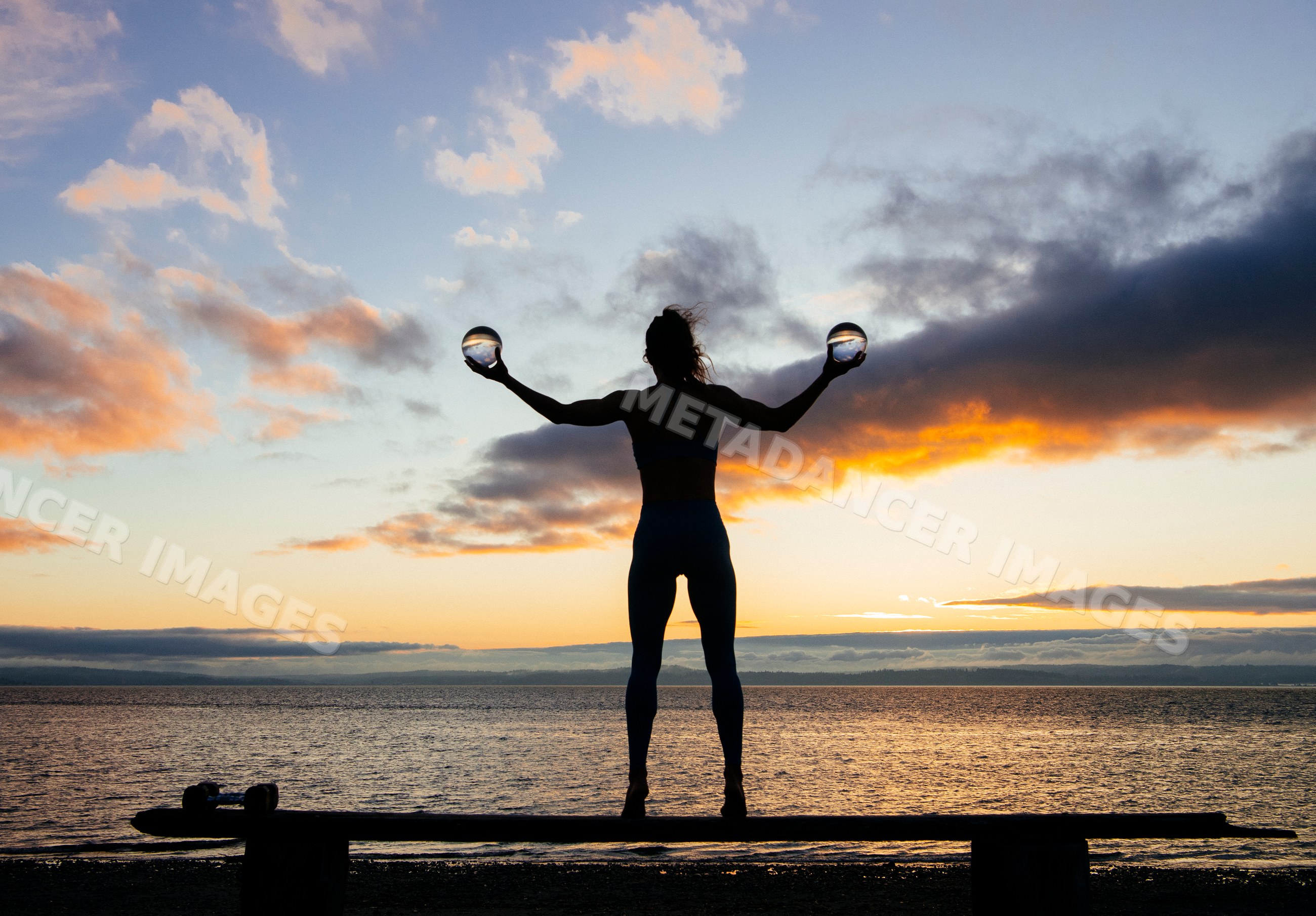 Silhouette of white woman balancing glass balls at sunset by lake