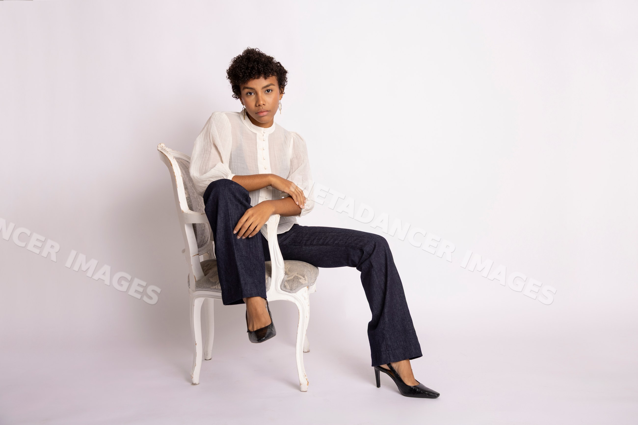 Hispanic woman posing on white chair in studio setting