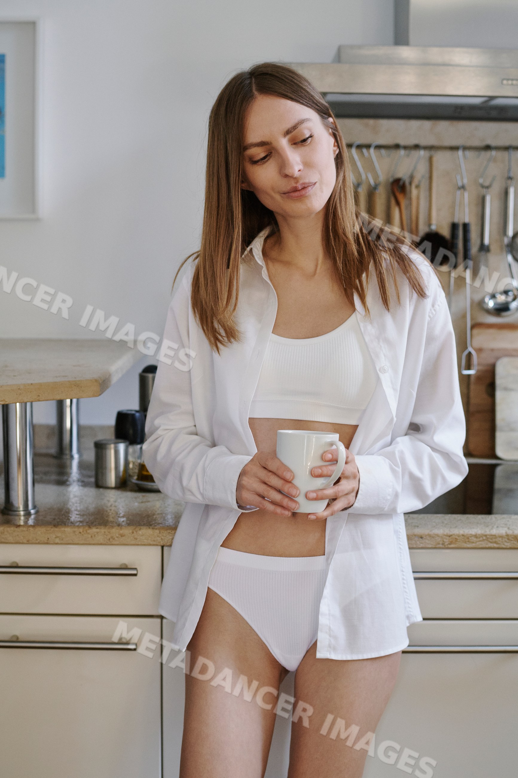 Woman in white underwear holds a coffee mug in a kitchen in Germany