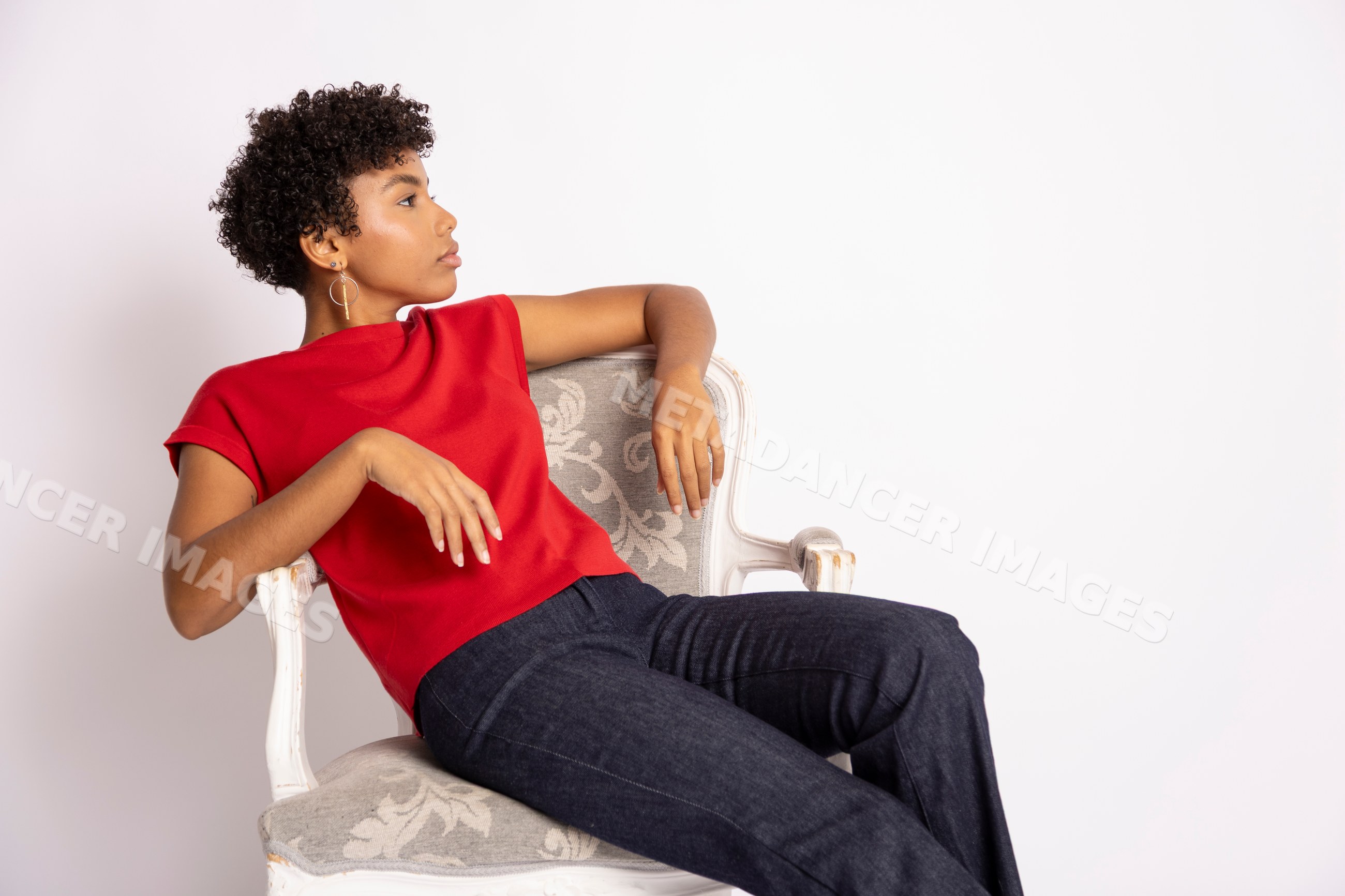 Hispanic woman wearing red top and jeans sitting on a decorative chair