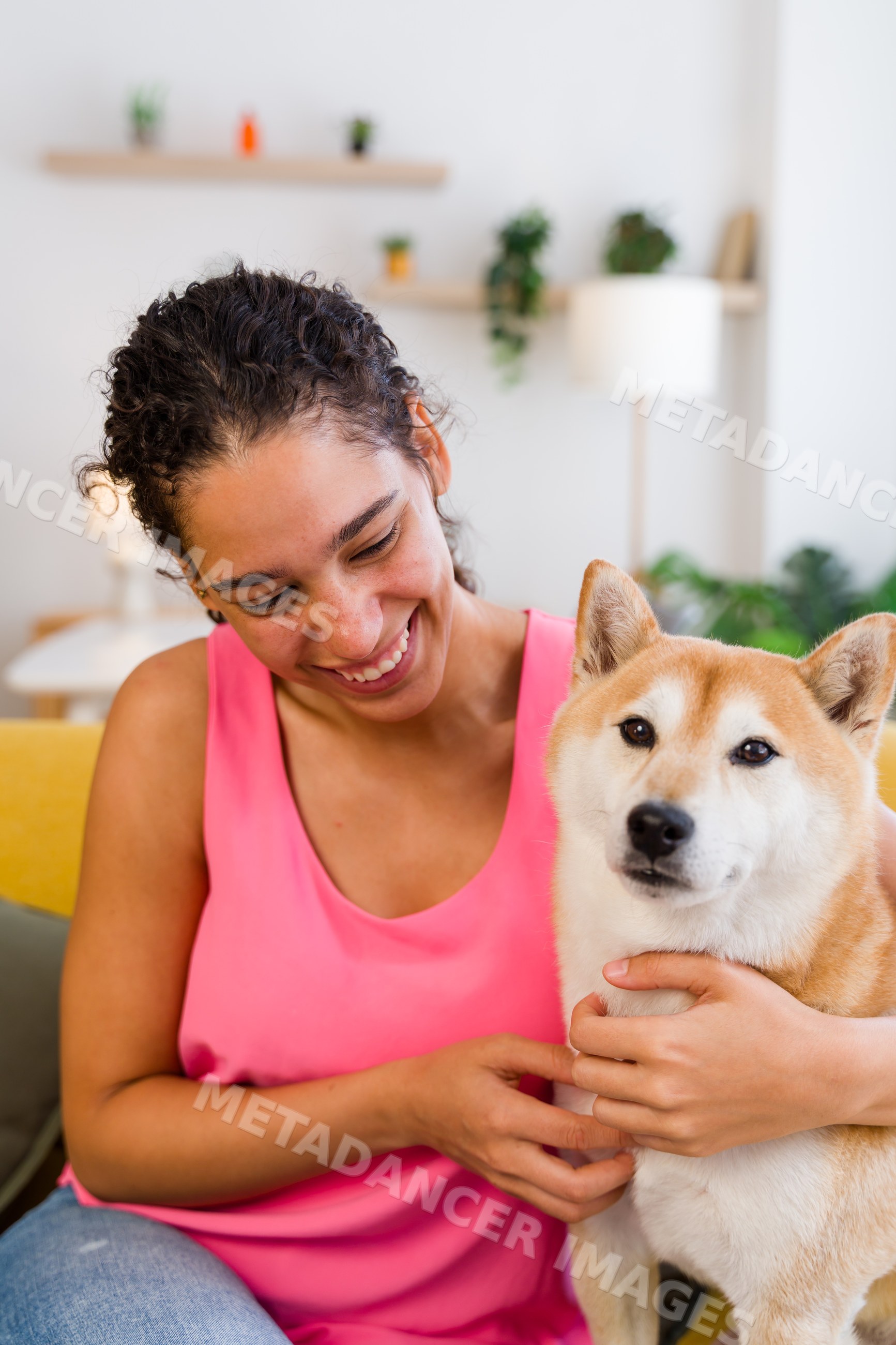 A Hispanic woman happily pets her dog indoors