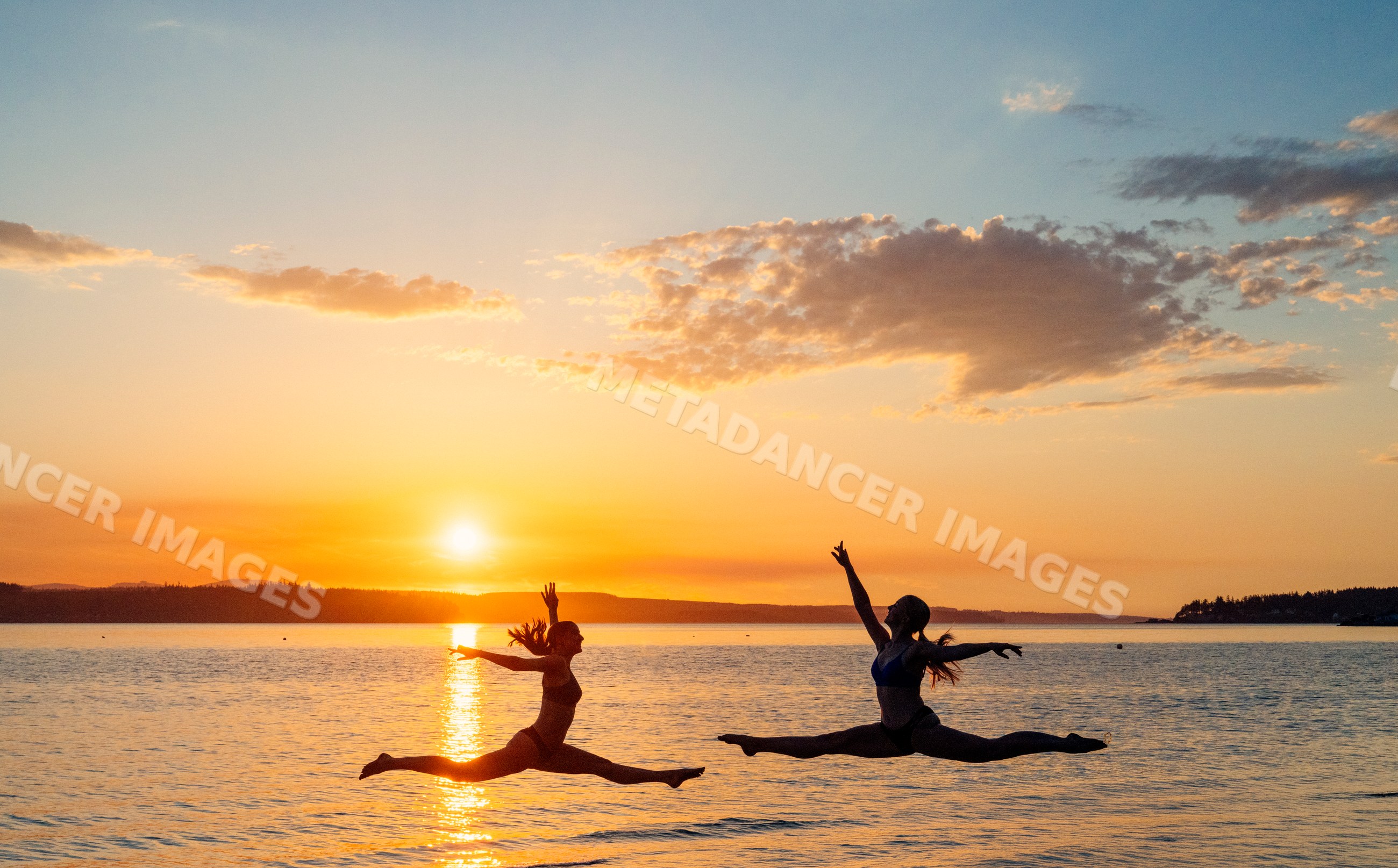 Two white women performing split leaps over water at sunset in WA, USA