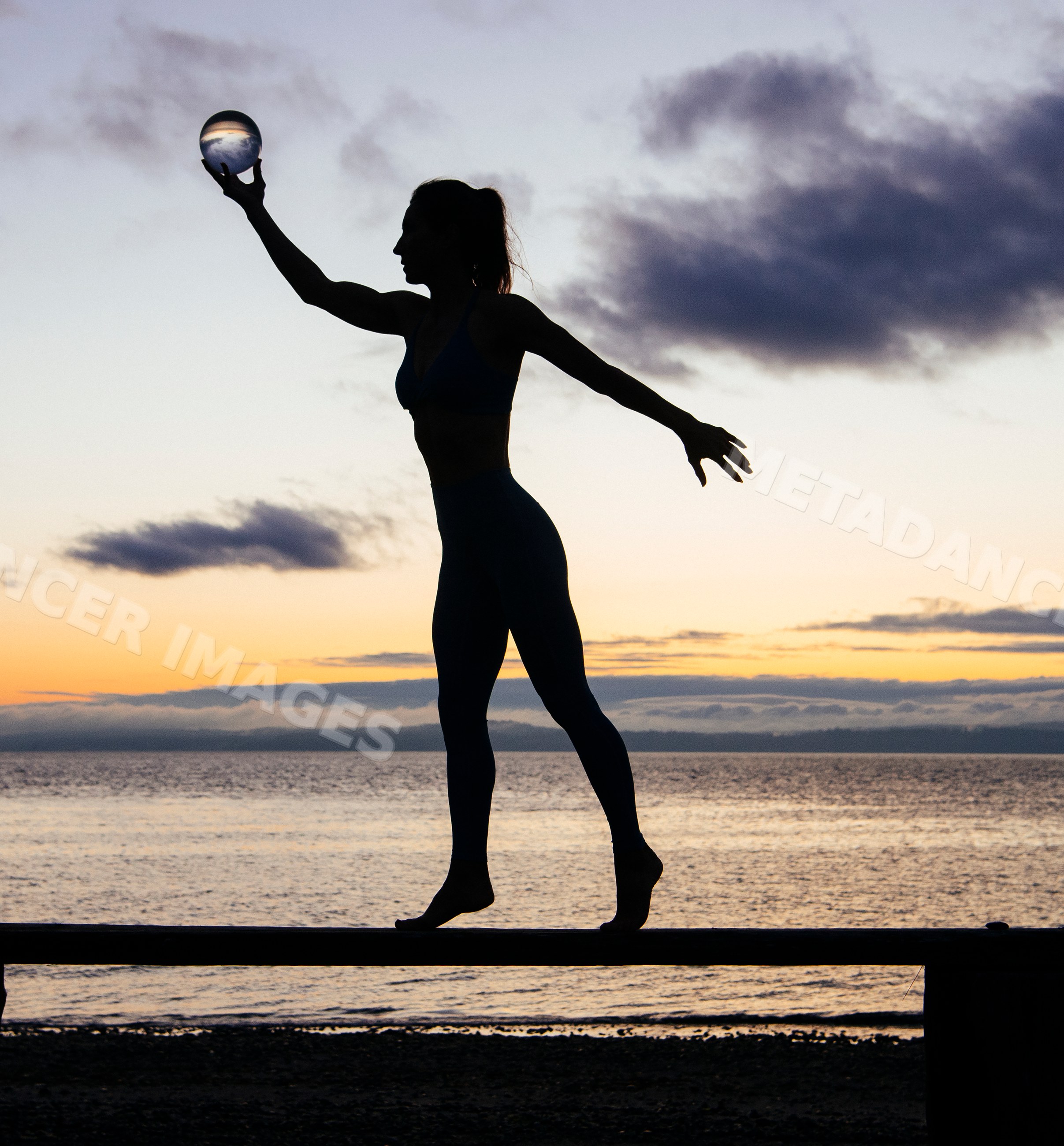 Silhouette of white woman balancing with crystal ball on beach