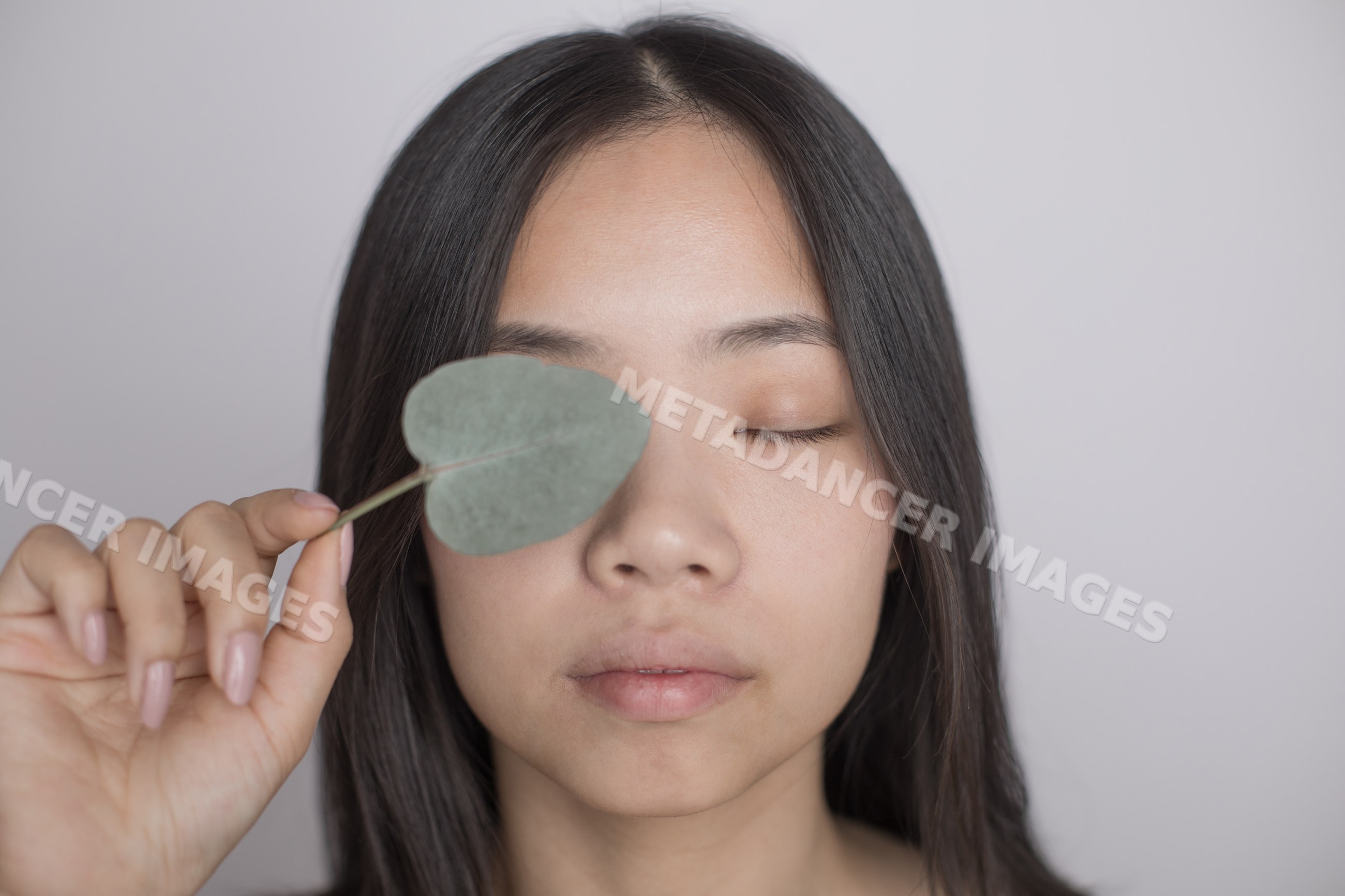 Calm Southeast Asian woman holding leaf over eye