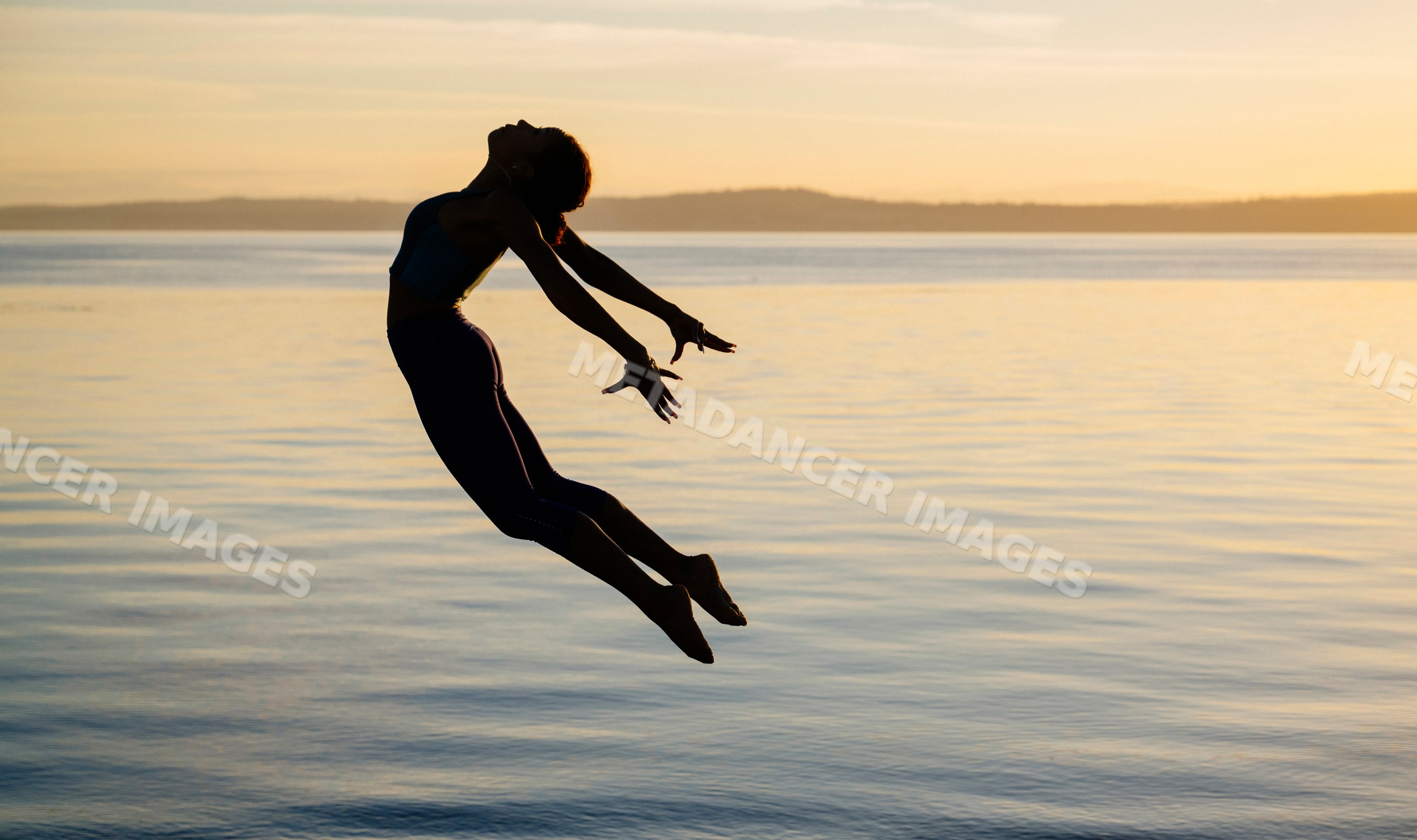 Hispanic woman leaping above bench by lake at sunset in the USA