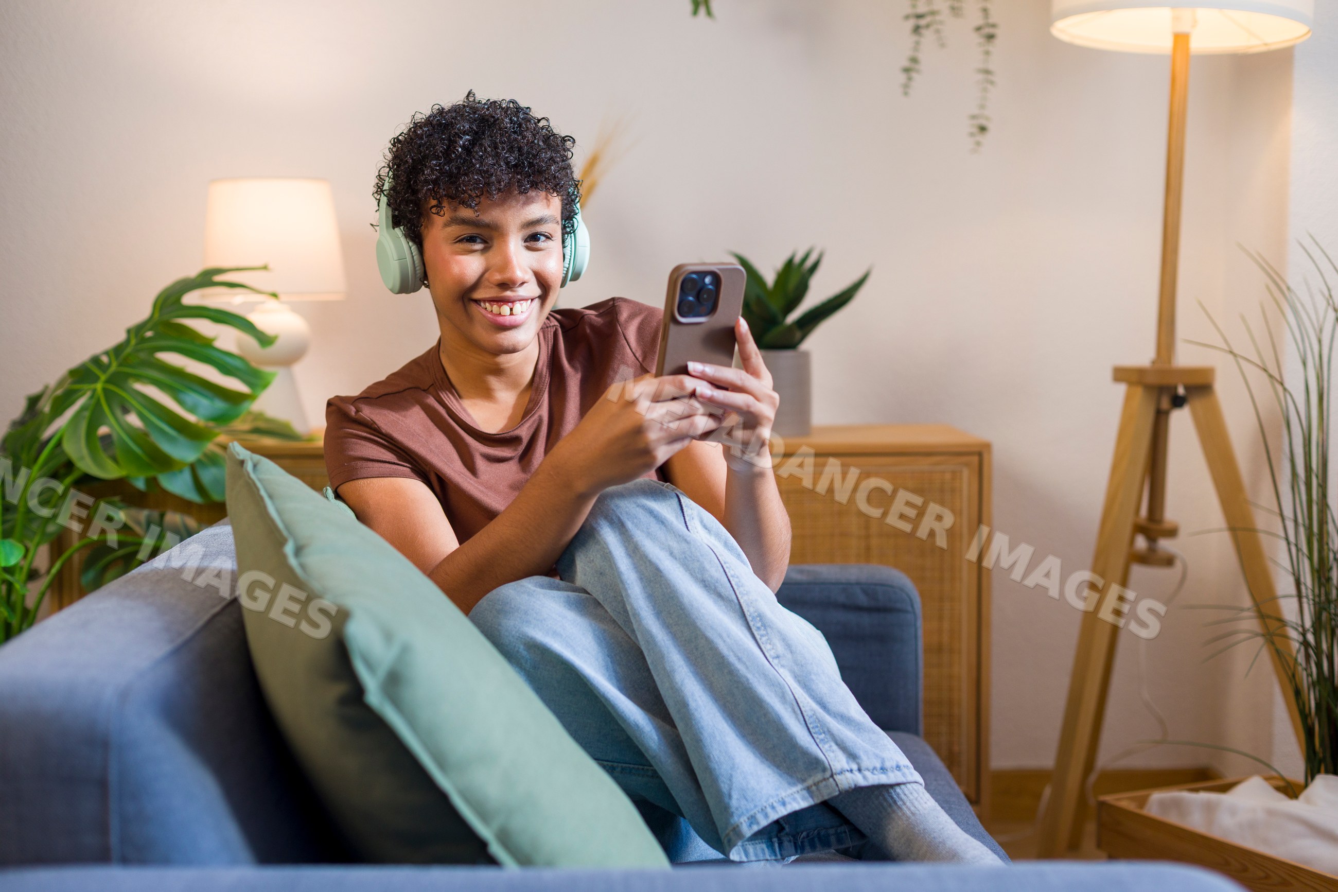 Young African American woman sitting on couch with headphones holding