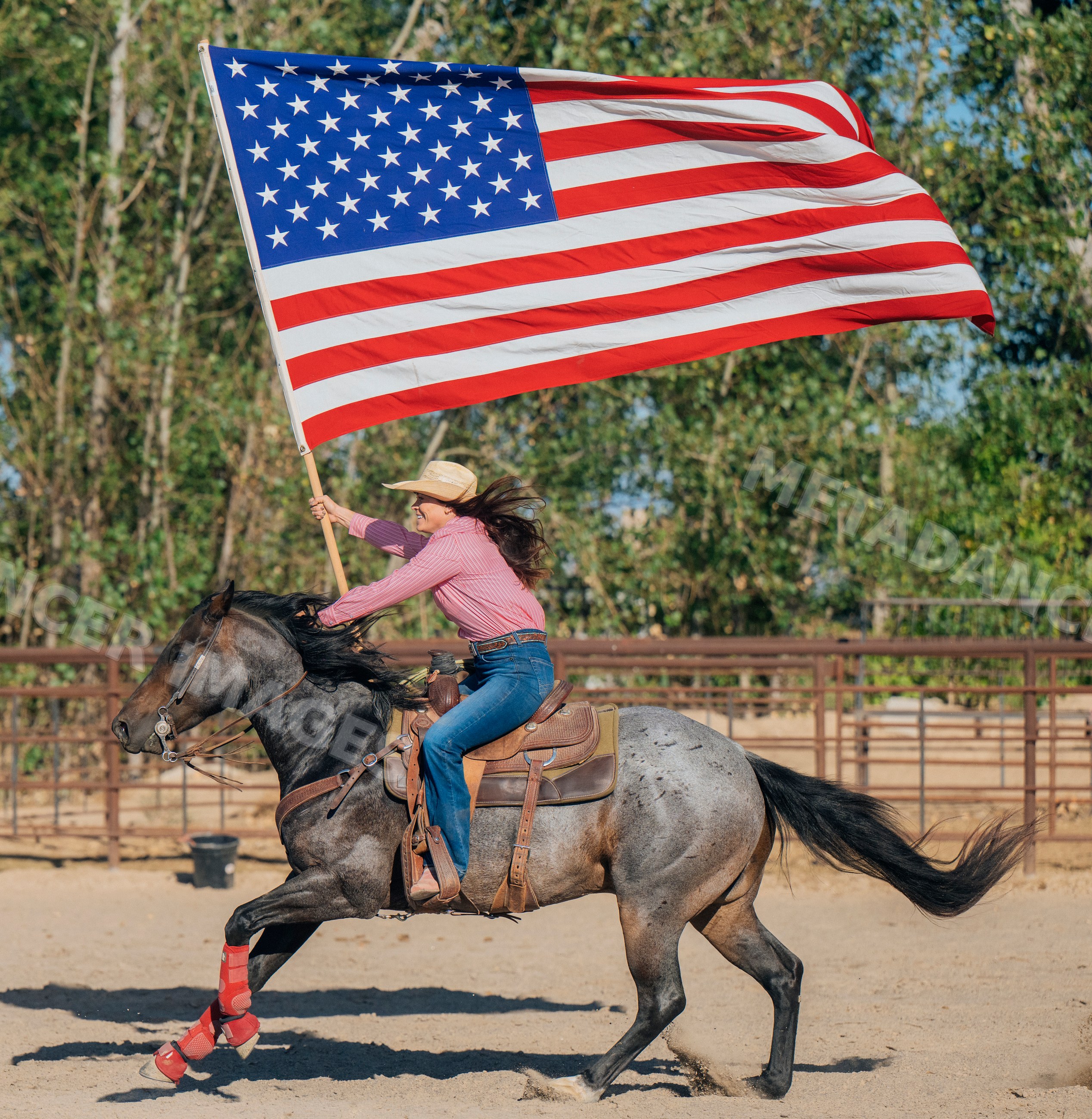 White woman rides galloping dapple gray horse holding american flag