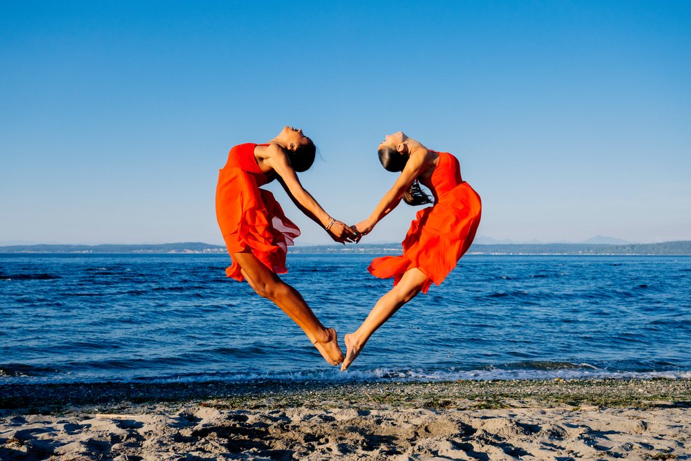 Two women jump holding hands performing partner acrobatics yoga