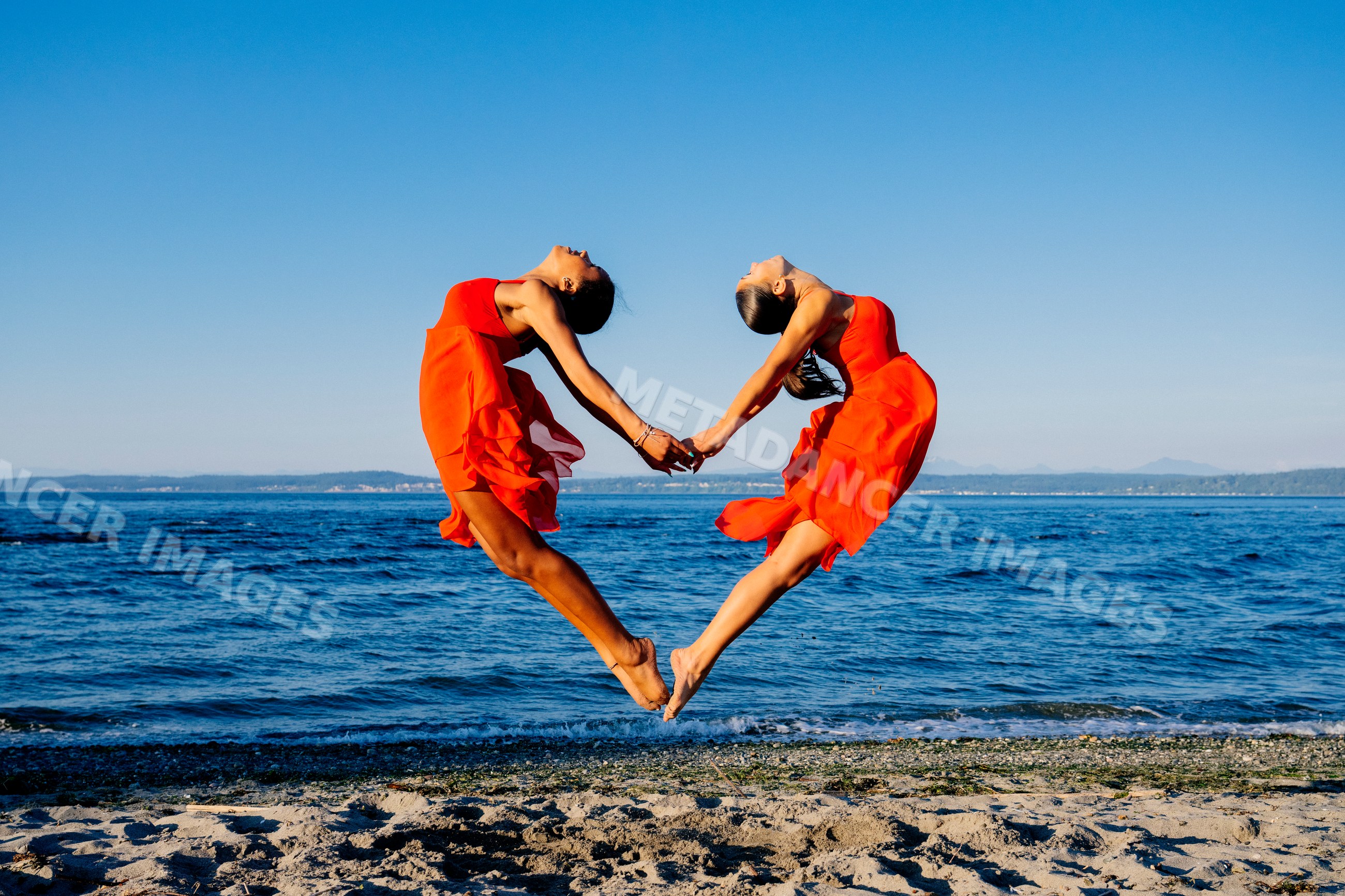 Two women jump holding hands performing partner acrobatics yoga