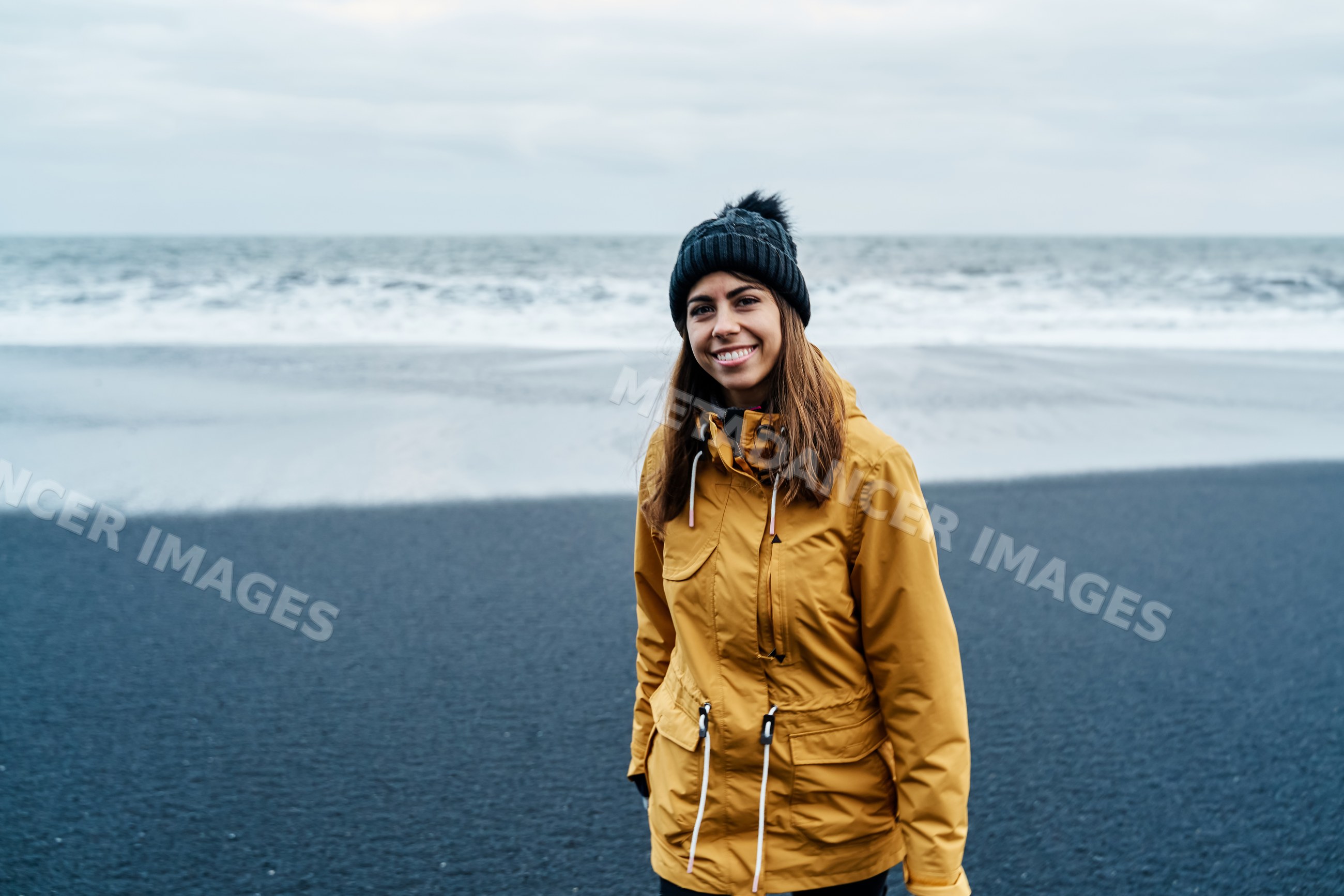 Smiling white woman in yellow jacket standing on black sand beach