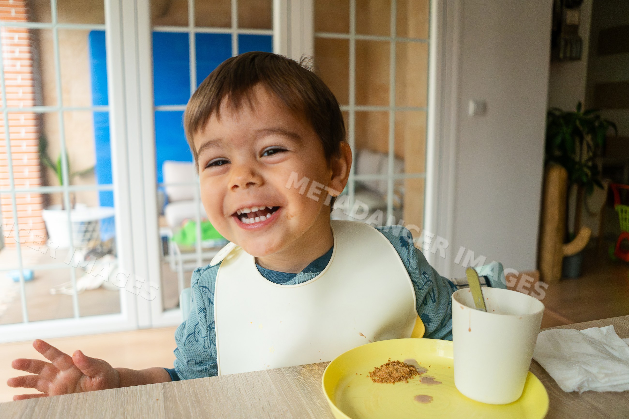 A toddler happily eating a snack indoors featuring a white model