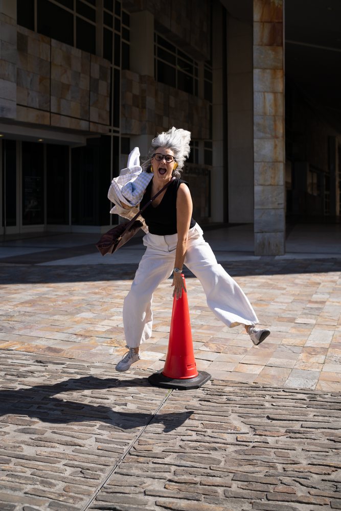 Joyful white woman jumping near red traffic cone on sidewalk