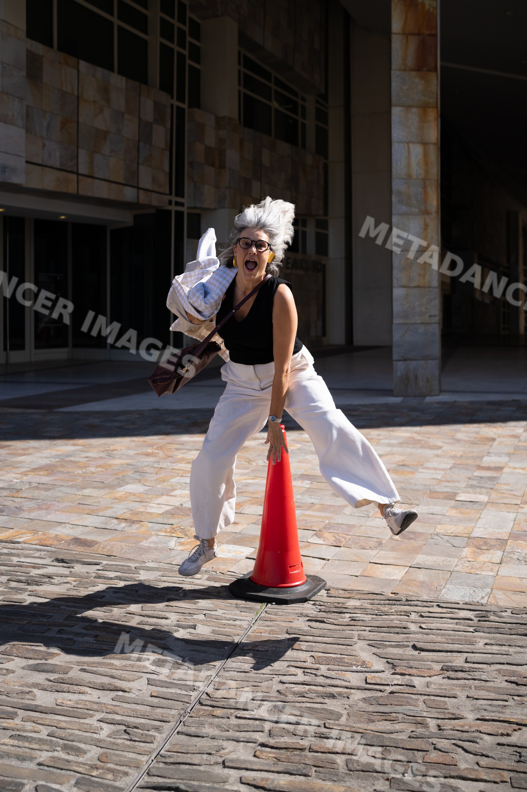 Joyful white woman jumping near red traffic cone on sidewalk