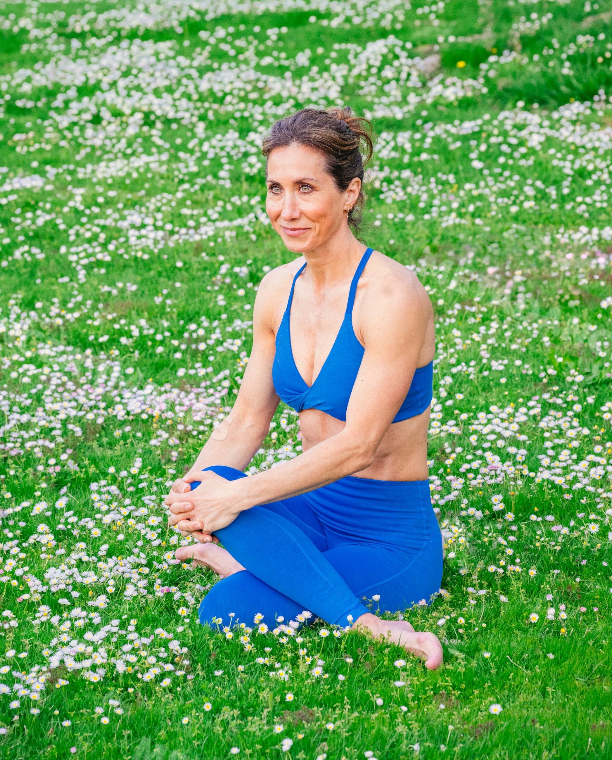 White woman practicing yoga outdoors on grassy field with flowers