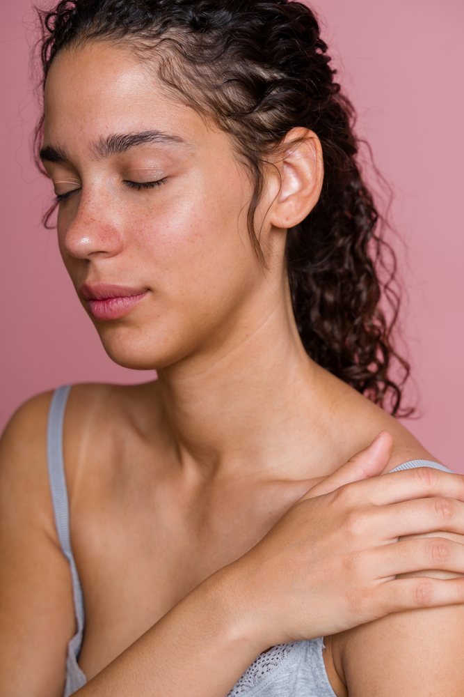 Hispanic woman with curly hair and closed eyes touching shoulder