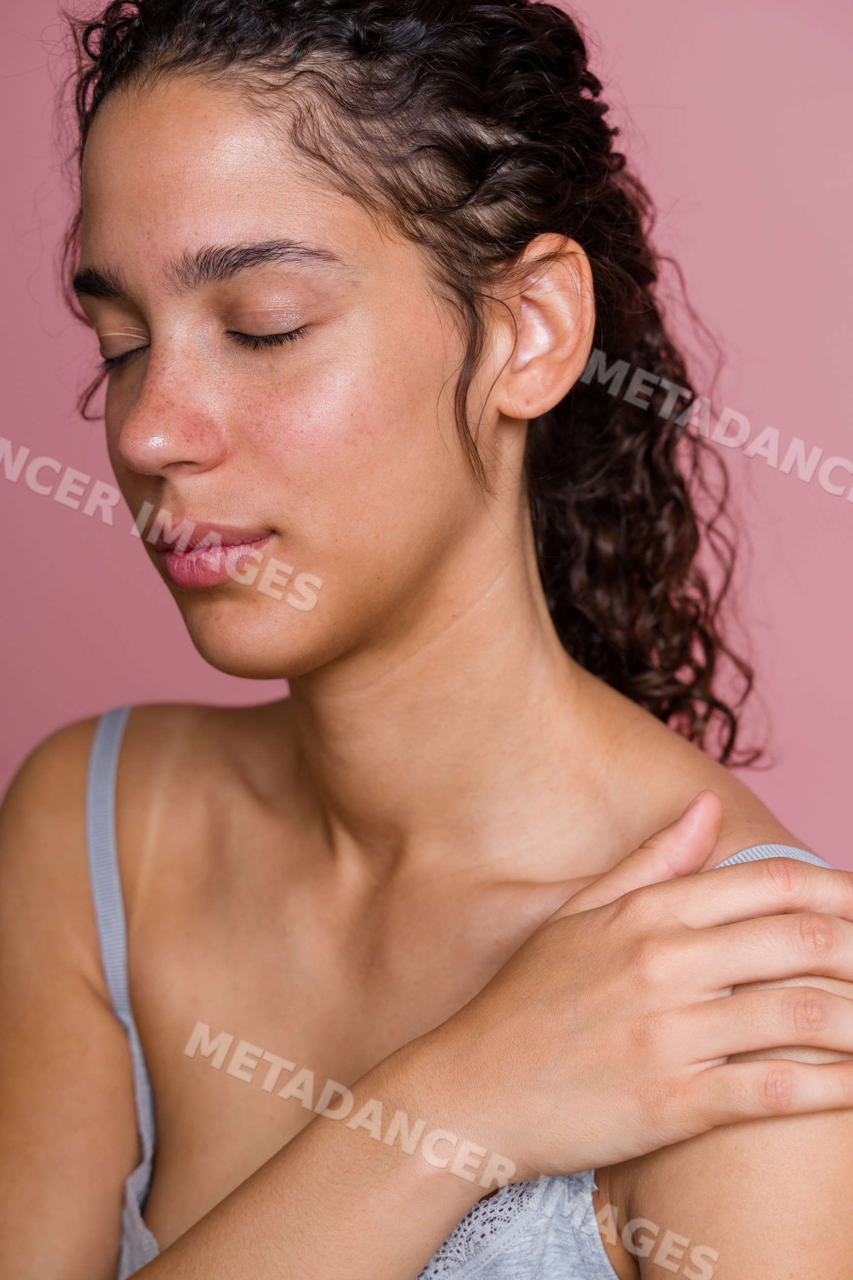 Hispanic woman with curly hair and closed eyes touching shoulder
