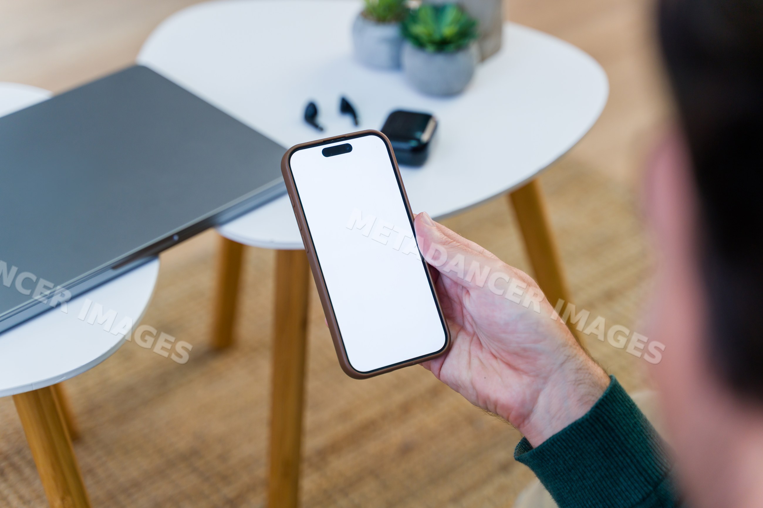 Smartphone held over white table with laptop and wireless earbuds