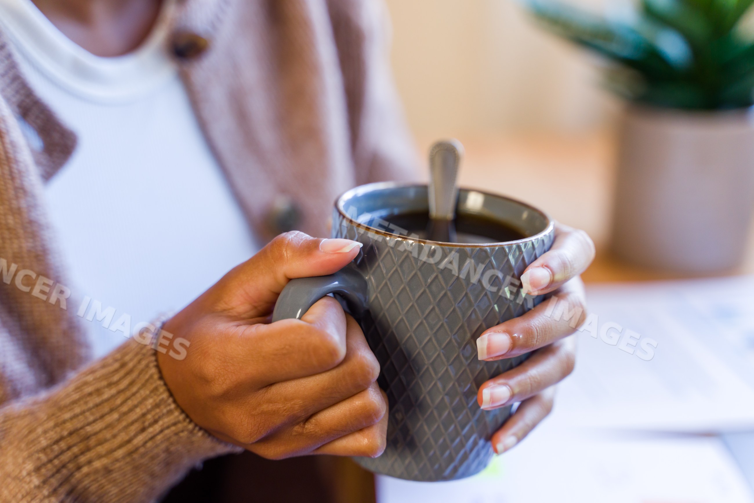 African American person holding mug of hot coffee indoors