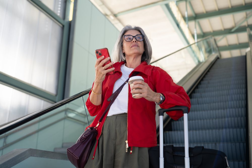 White woman waiting with luggage and coffee at airport escalator