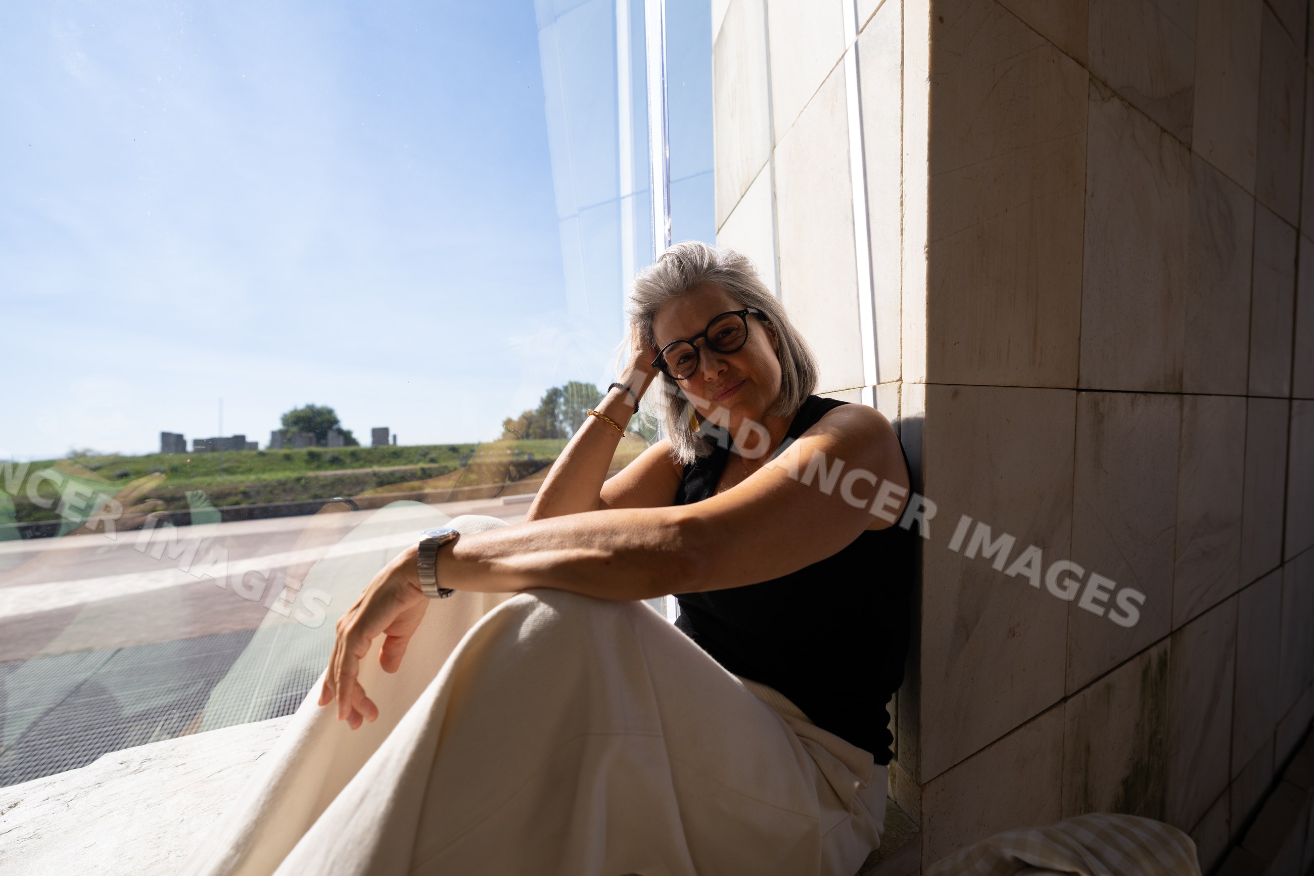 White woman sitting by window inside modern building with urban view
