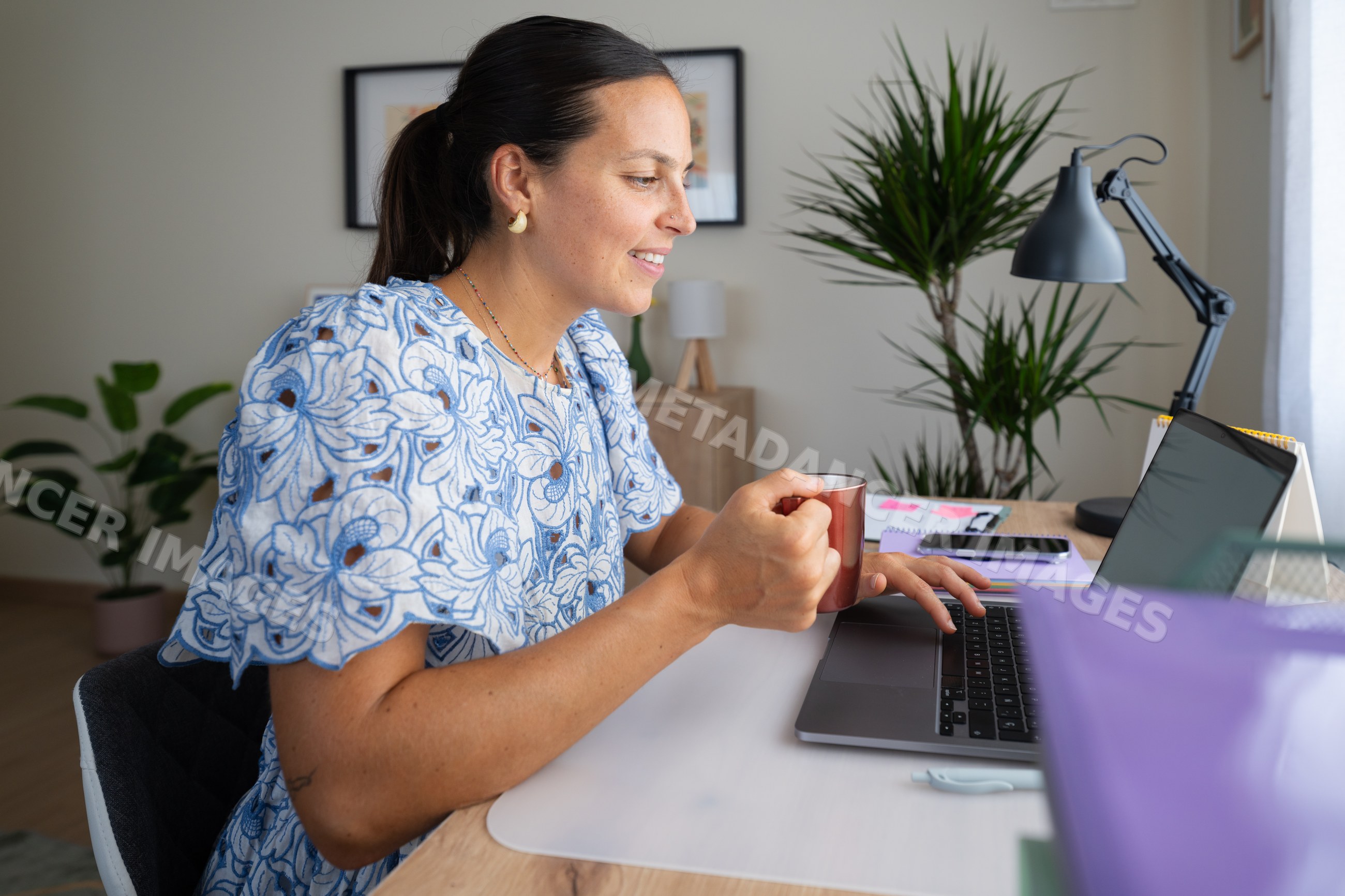 White woman working on laptop and drinking coffee in home office