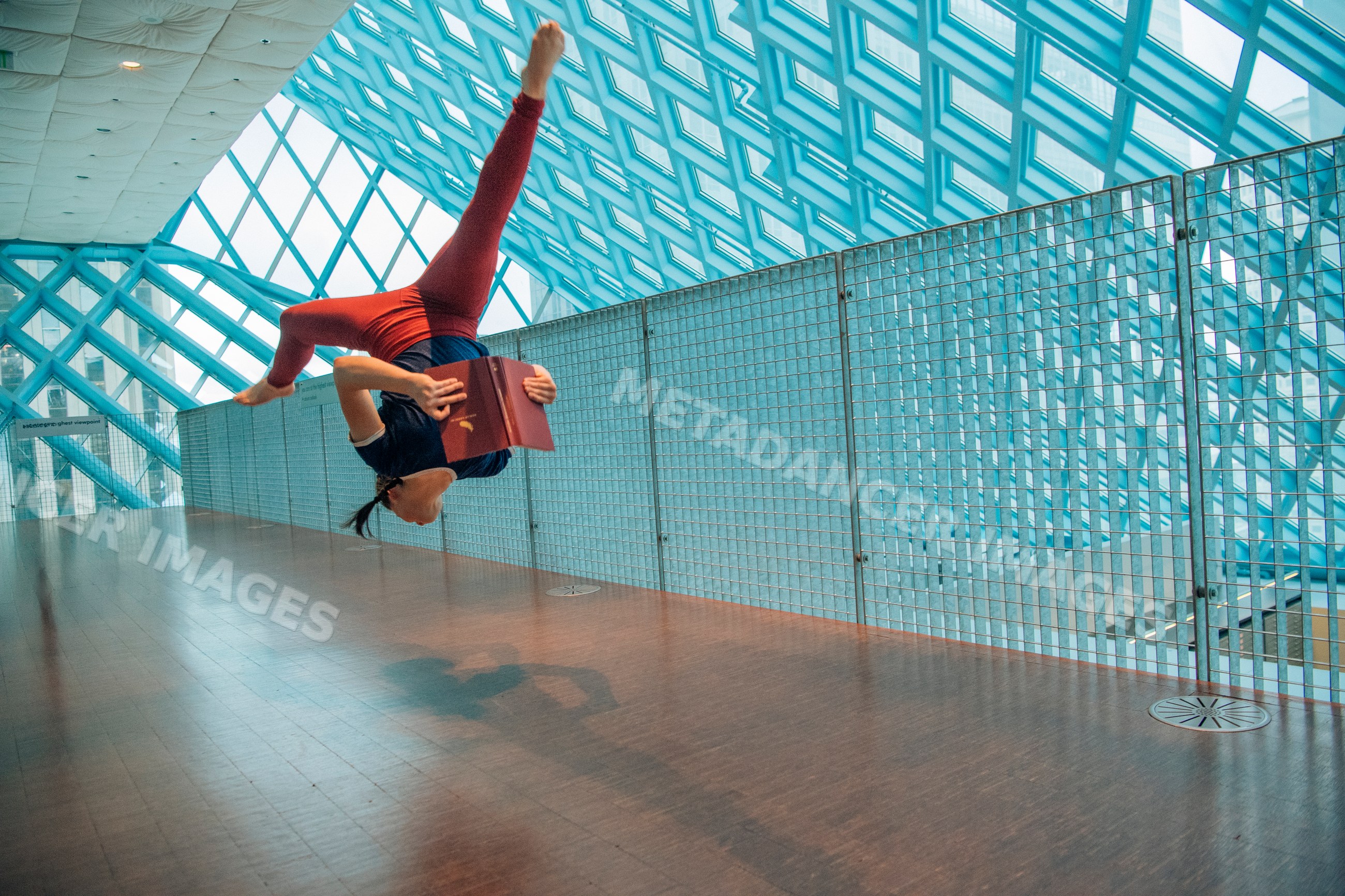 A woman performing a backflip while reading a book in a library