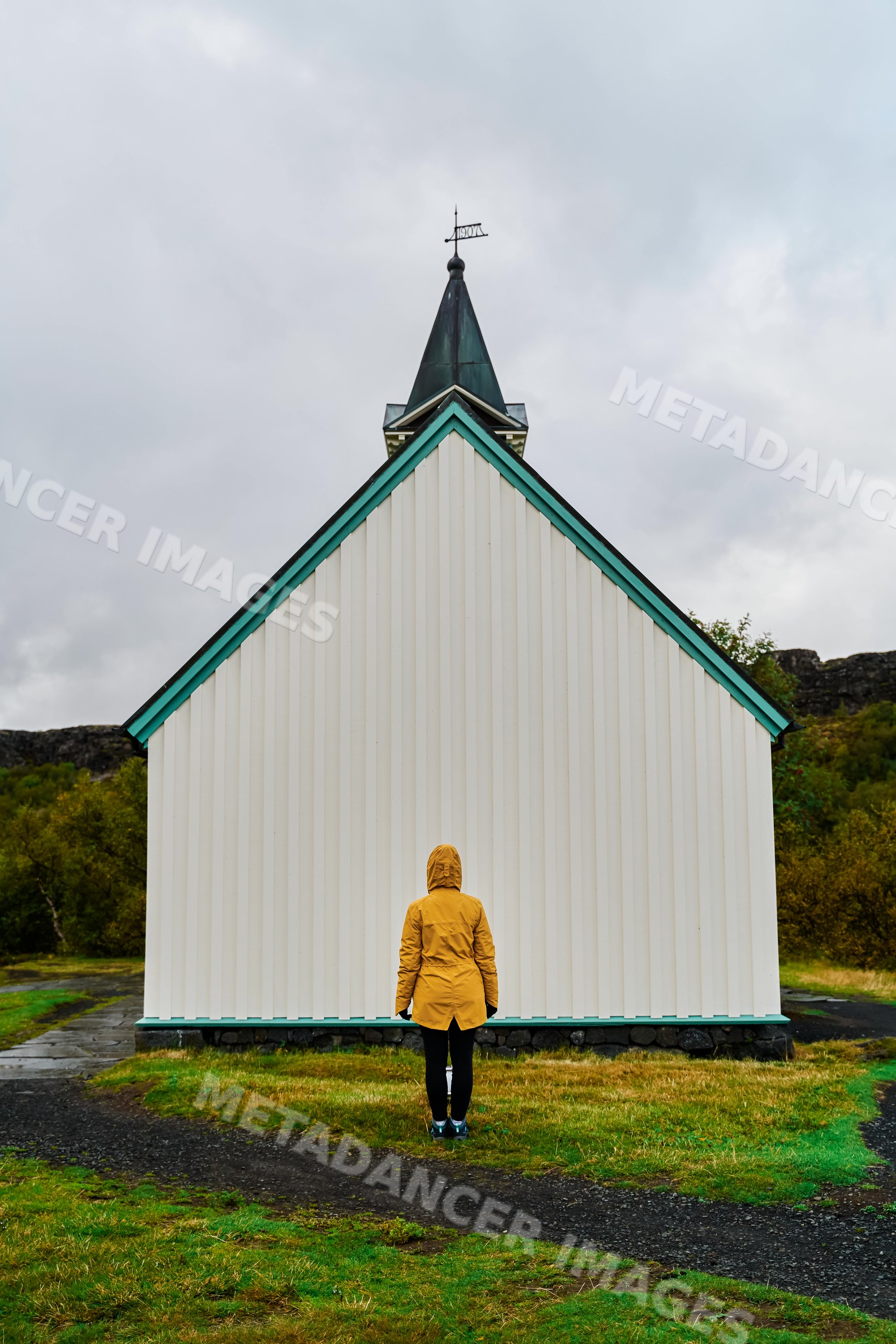 A person in a yellow jacket faces a small white church with steeple