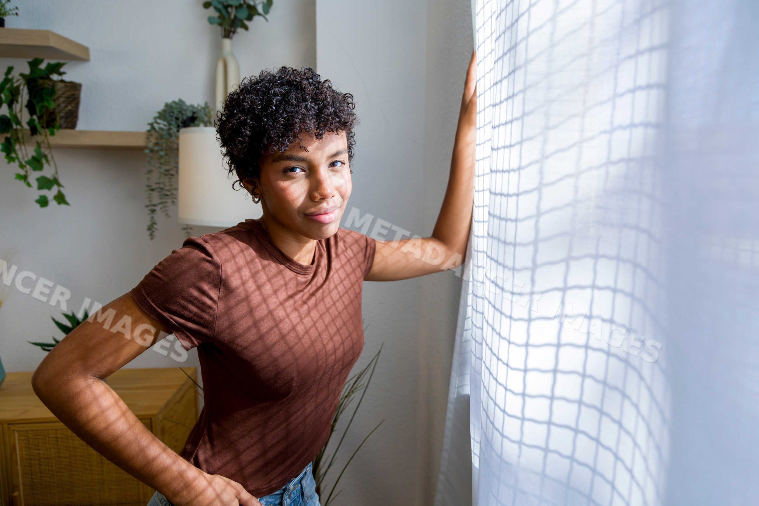 Young African American woman standing by window inside home interior