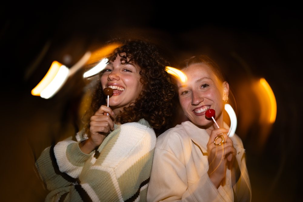Two white women laughing with lollipops and light trails at night