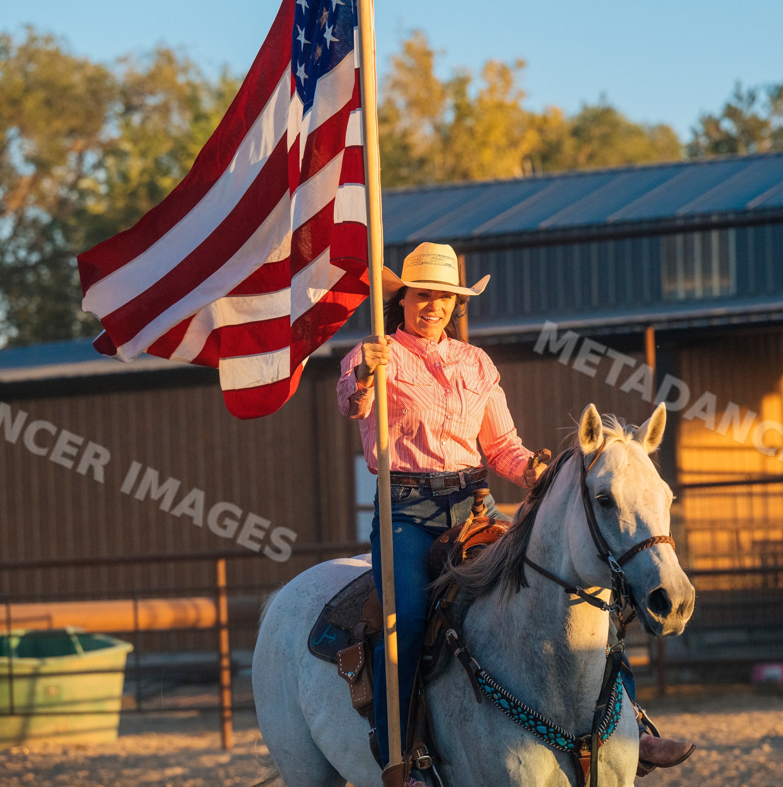 Woman riding white horse holding american flag near stable outdoors