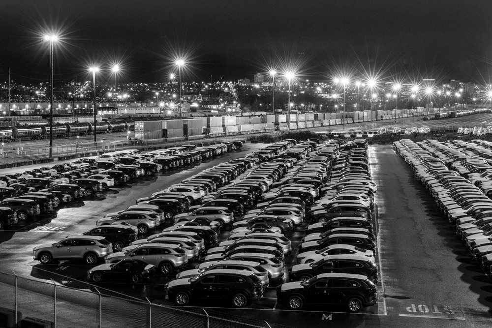 Large parking lot with parked cars and railway cargo containers