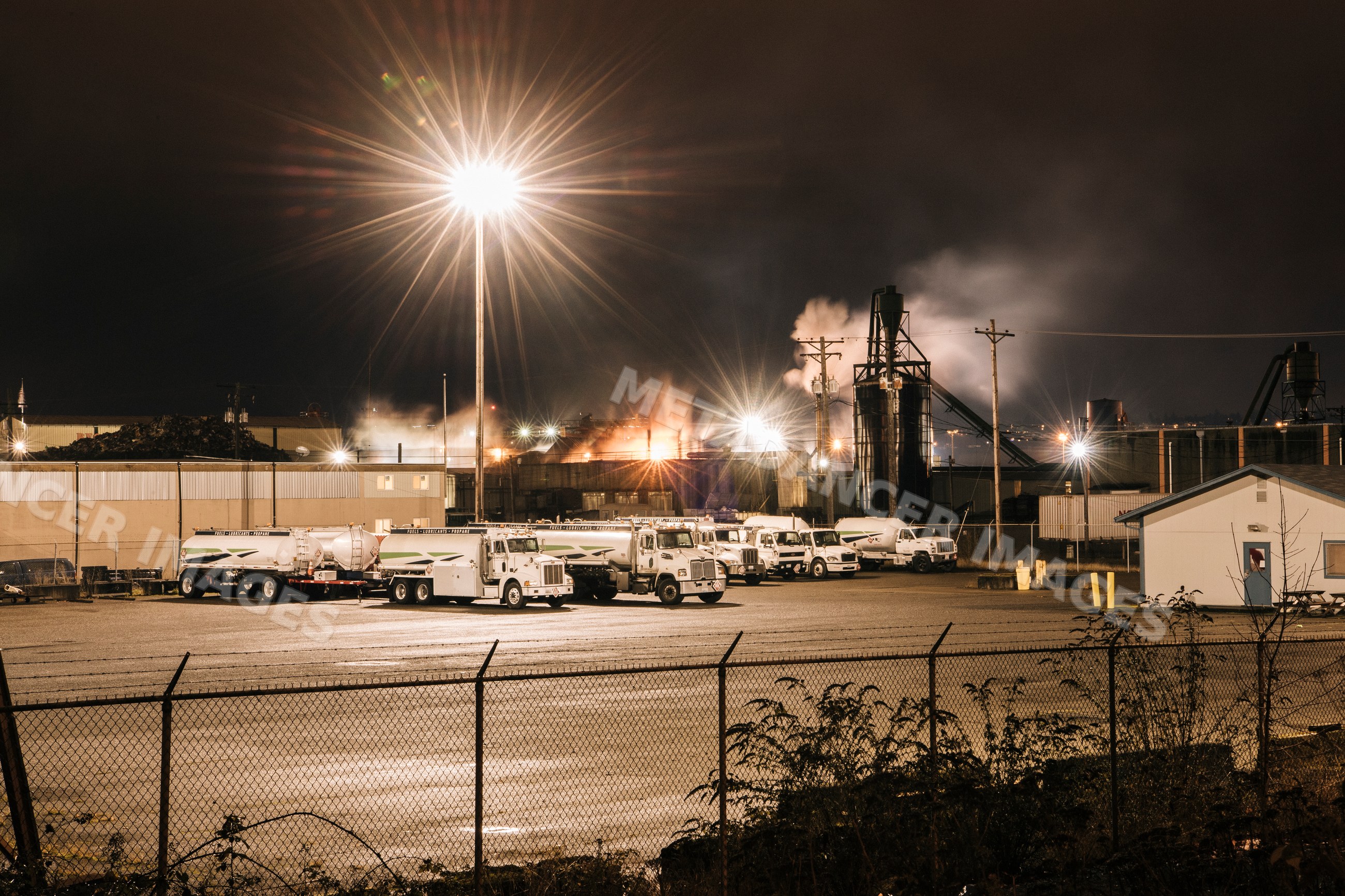Industrial plant with tank trucks and bright floodlight at night