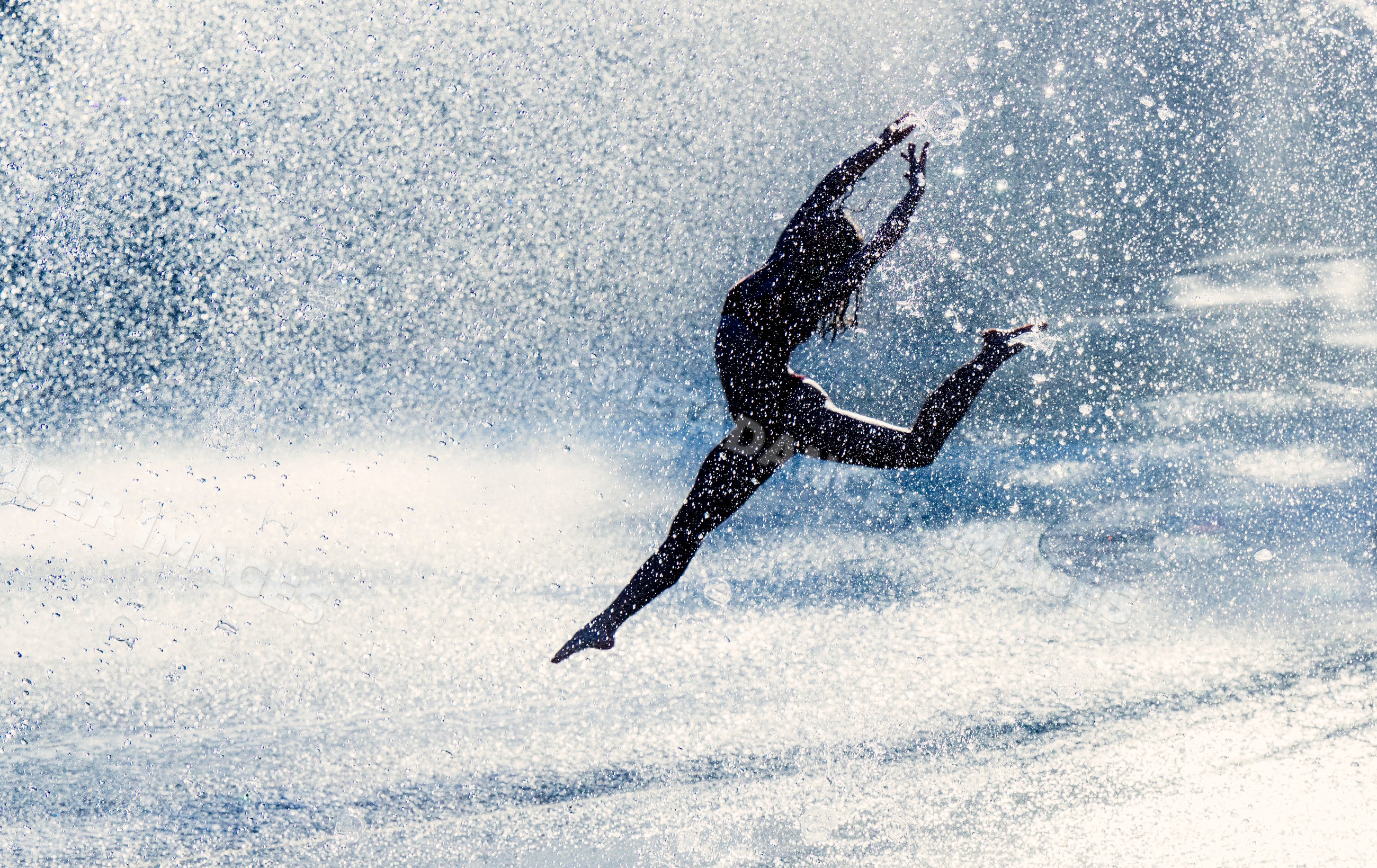 White woman jumping in water spray performing acrobatic yoga pose