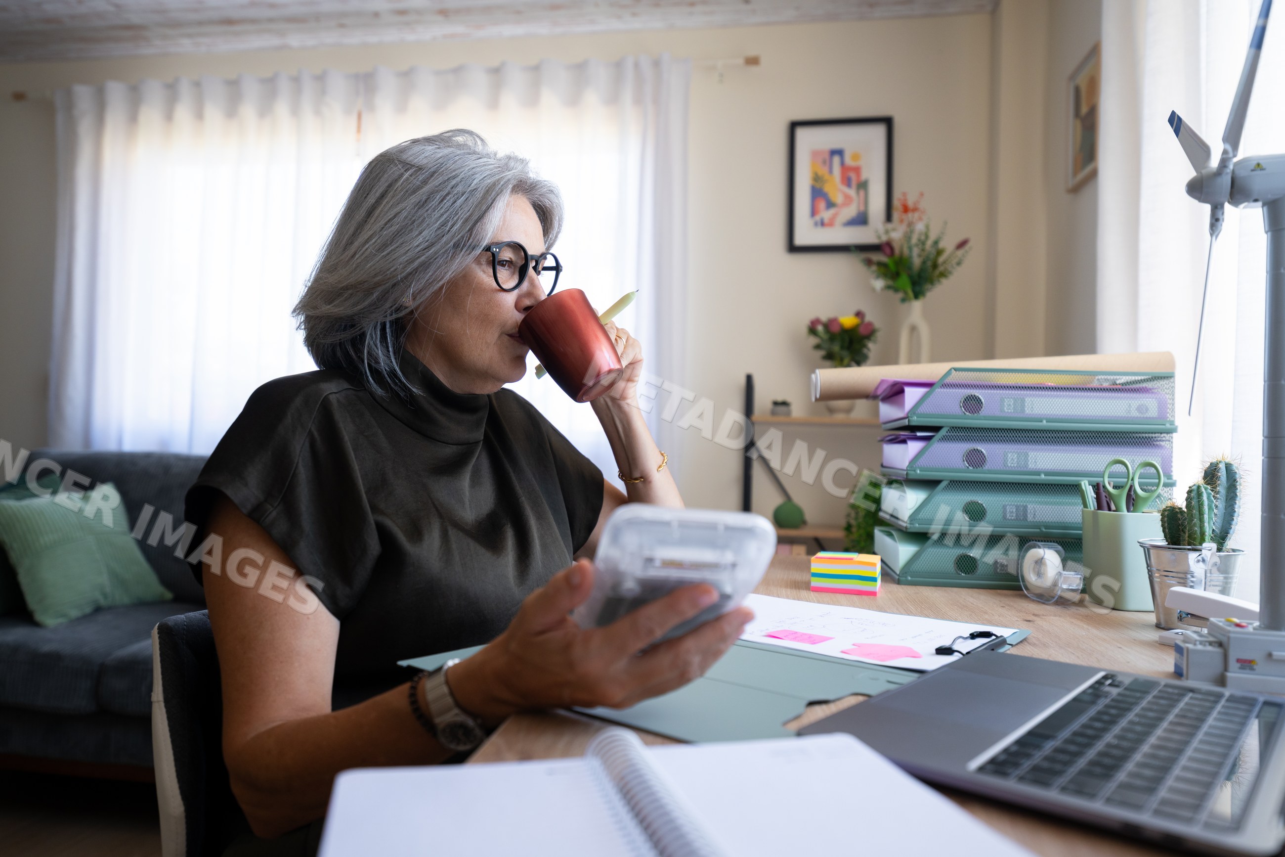 White woman drinking coffee while working at desk in home office
