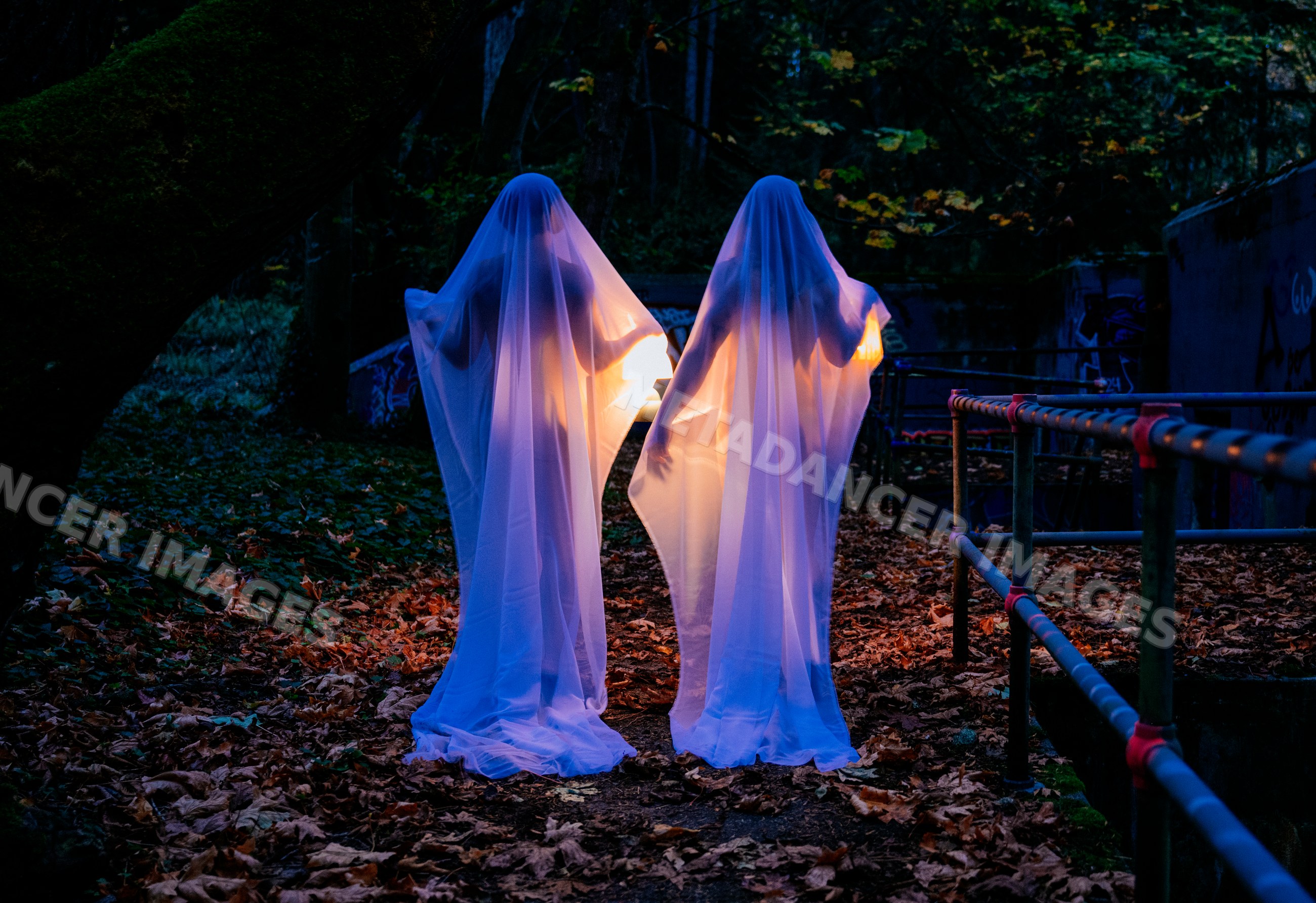 Two ghost figures holding glowing lights on forest path at night