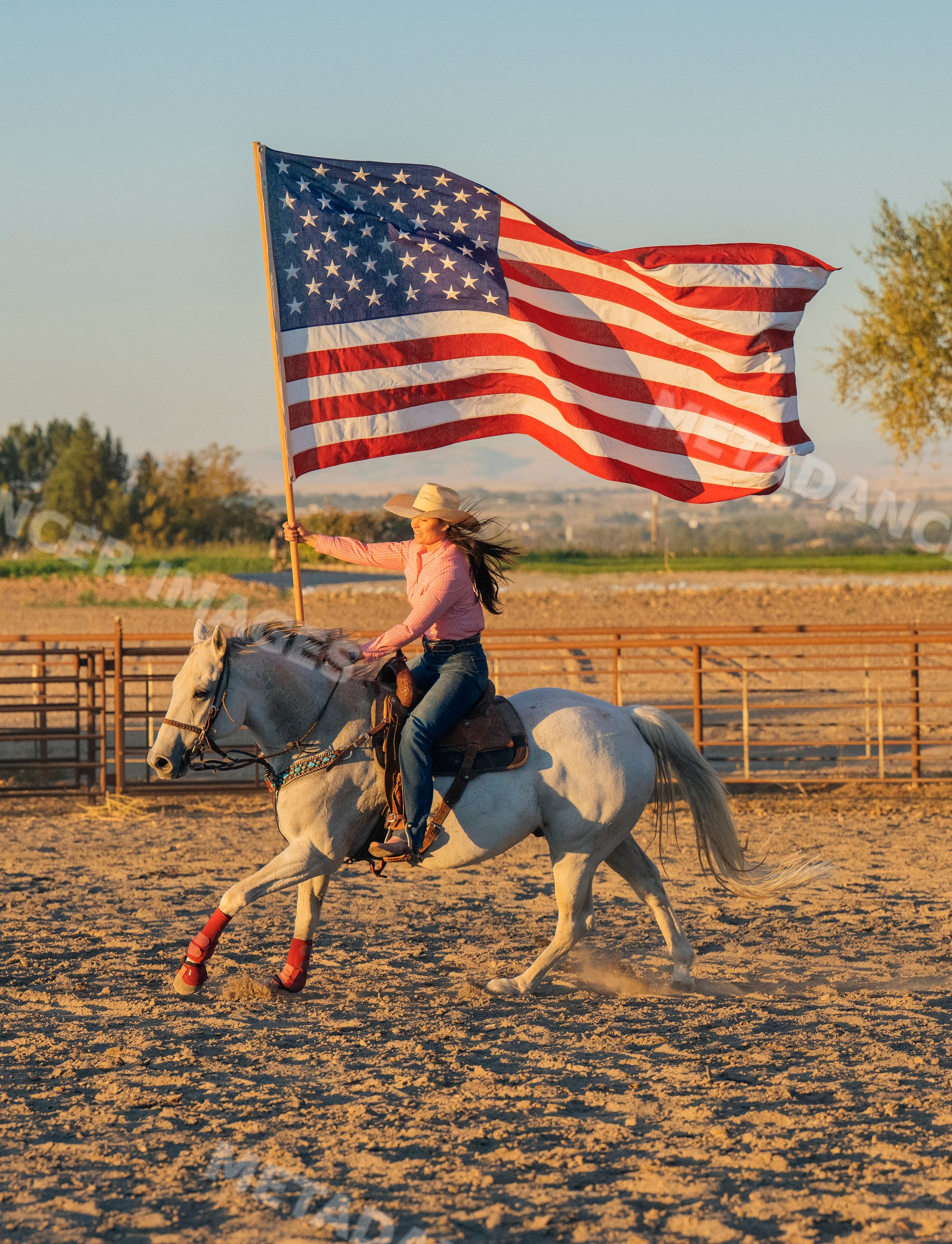 Woman riding white horse holding american flag in outdoor arena