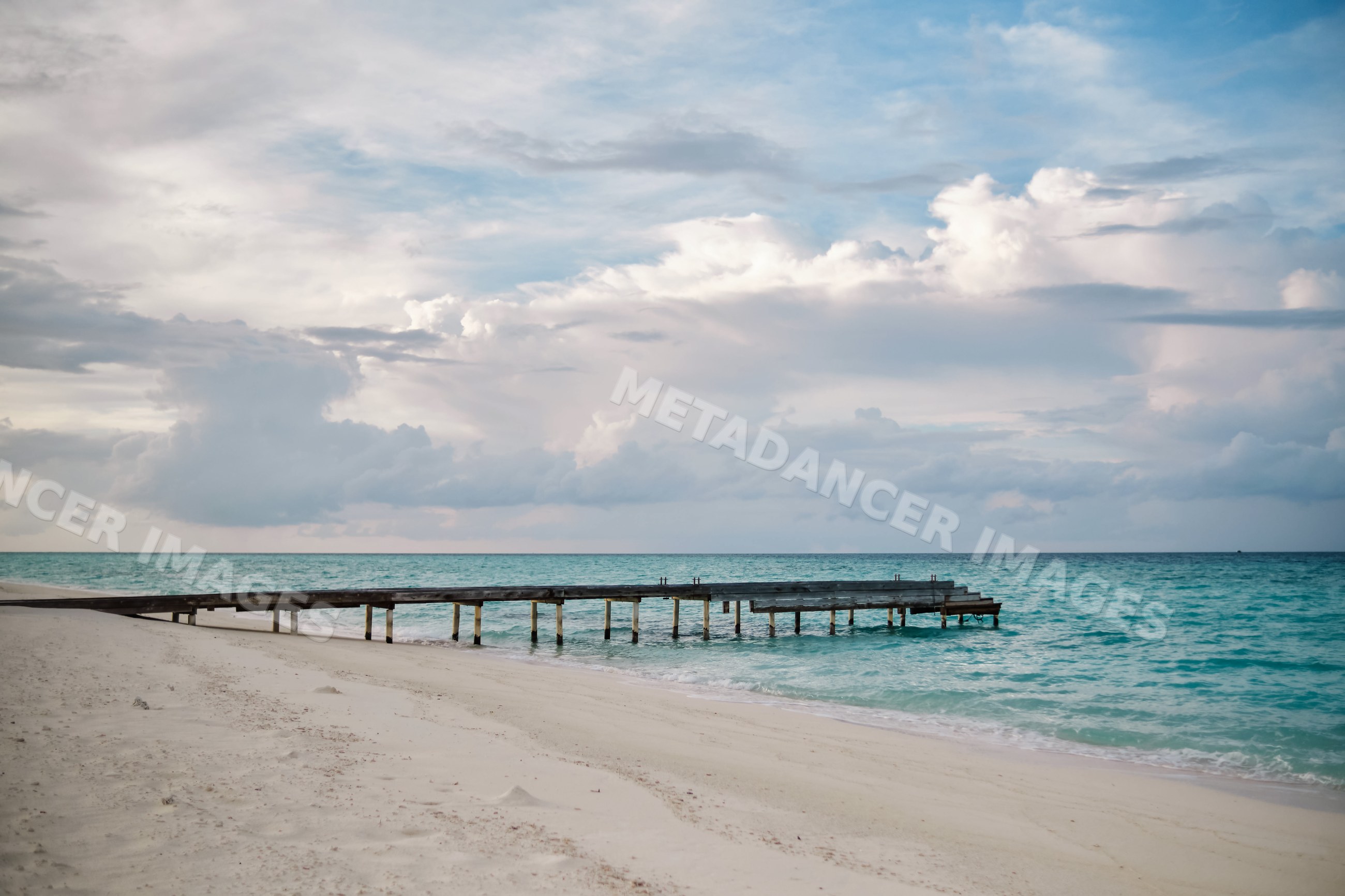 Wooden pier on a turquoise ocean beach with cloudy sky in a beach