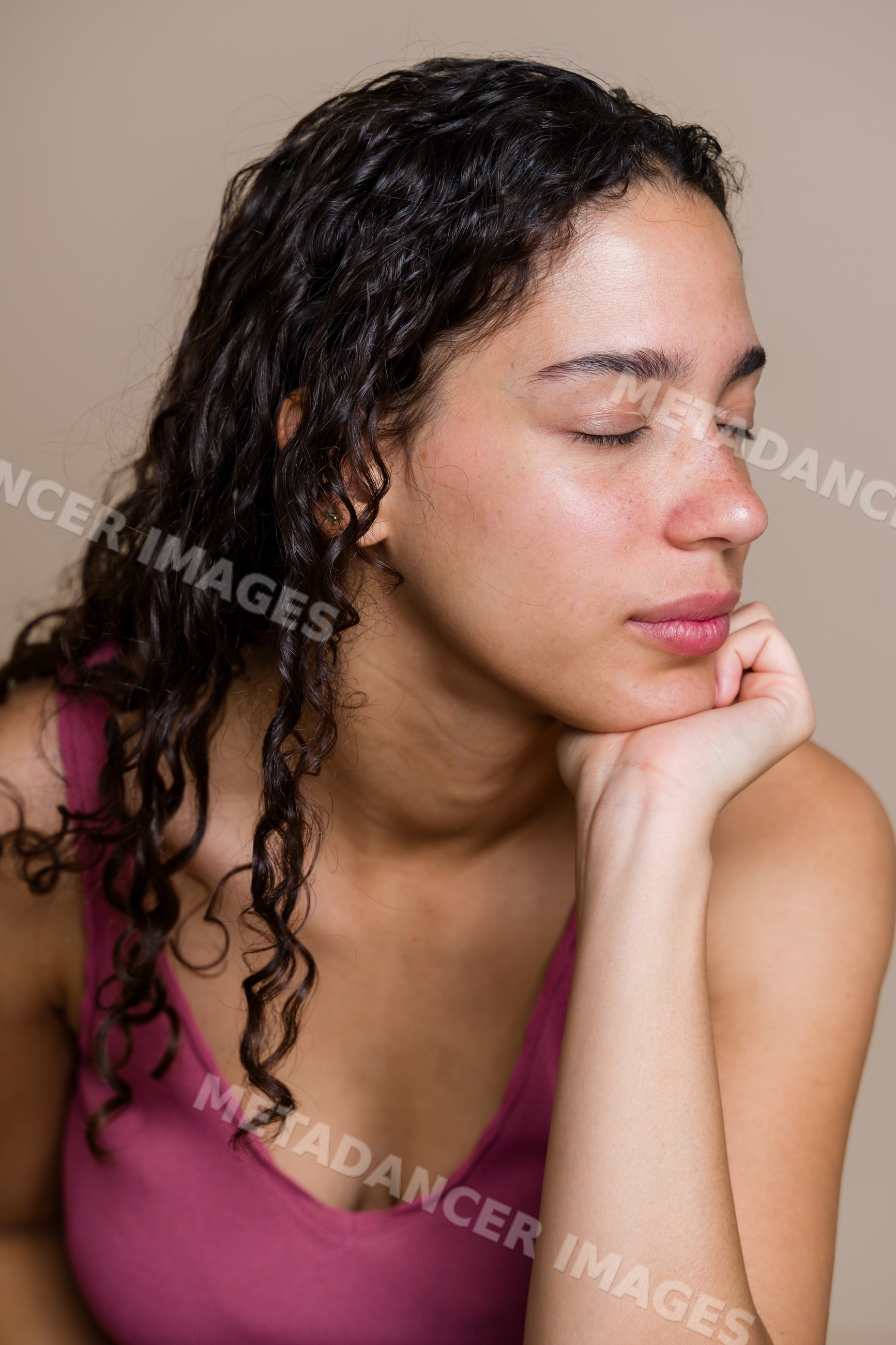 Hispanic woman with curly hair resting chin on hand with closed eyes