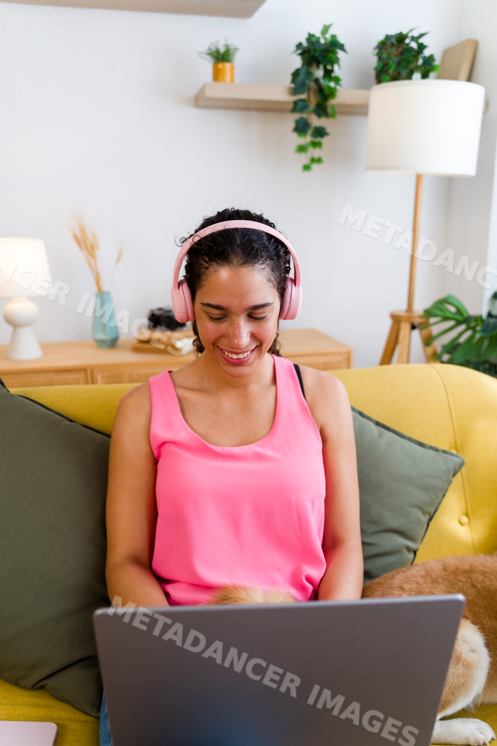 A Hispanic woman wearing pink headphones enjoys using a laptop
