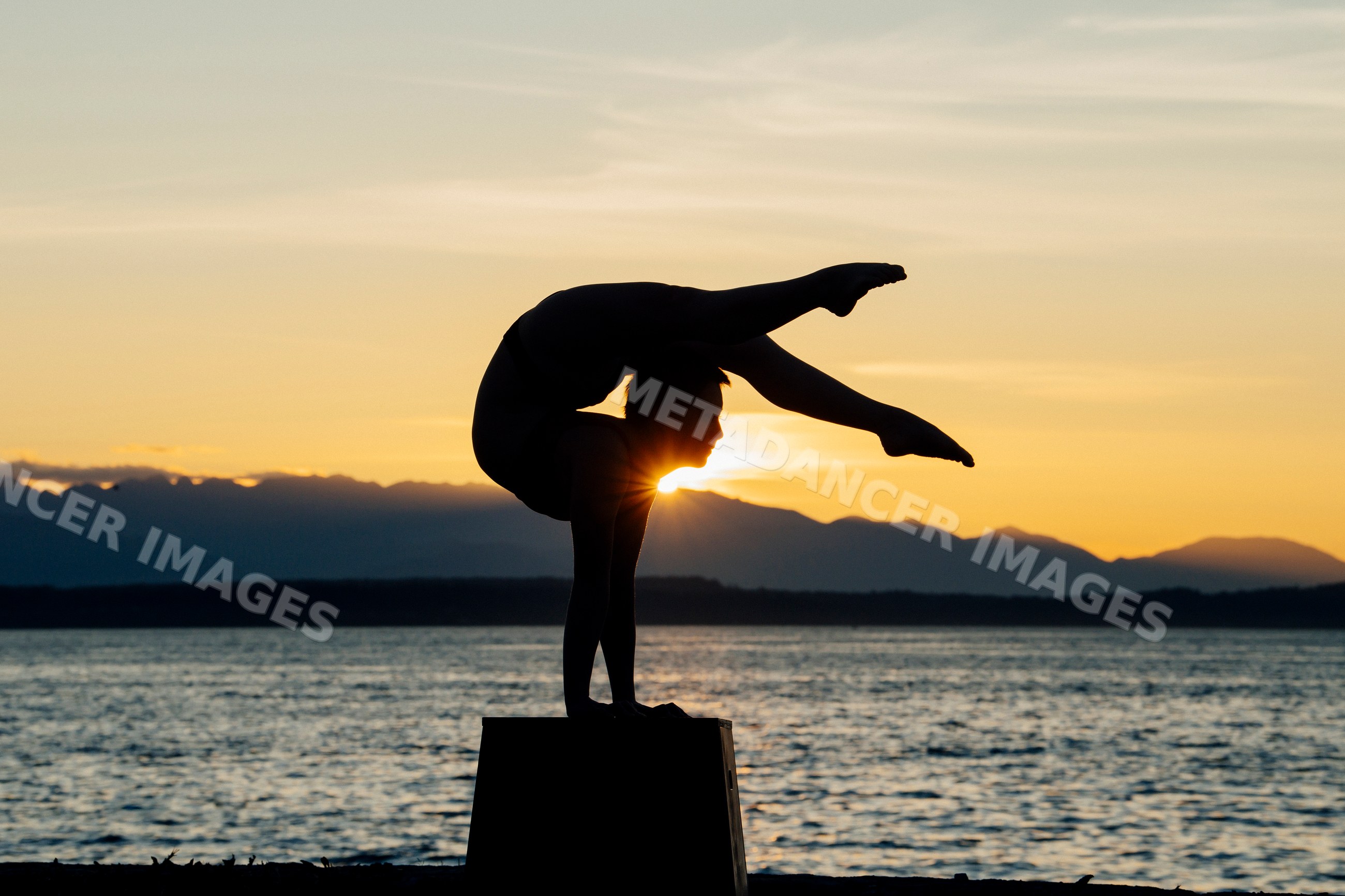 Yoga handstand silhouette at sunset by mountain lake