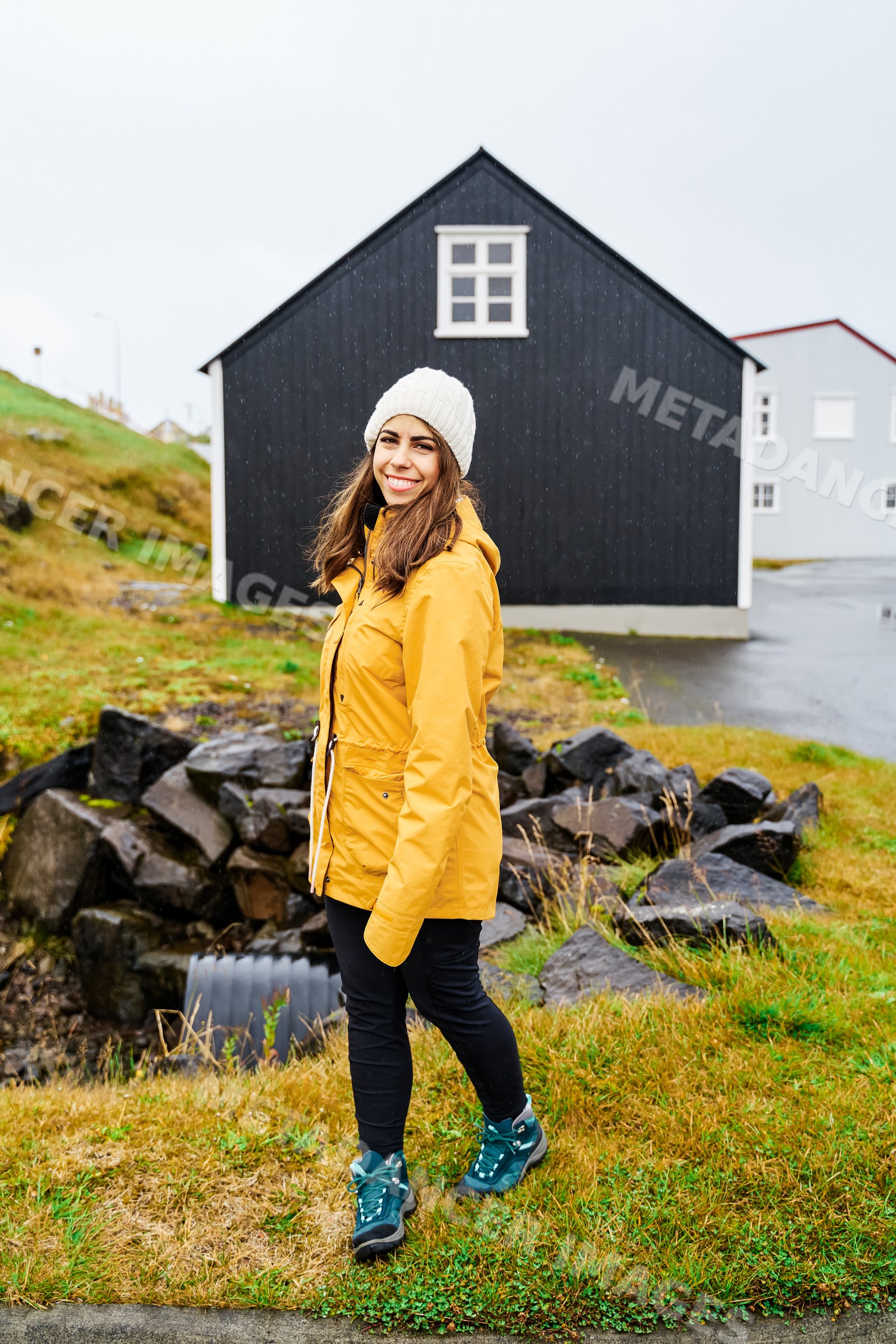 A white woman wearing a yellow jacket walks outside by a black house