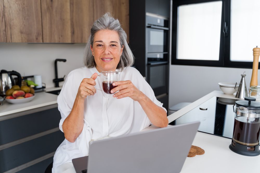 Middle aged white woman drinking coffee using laptop