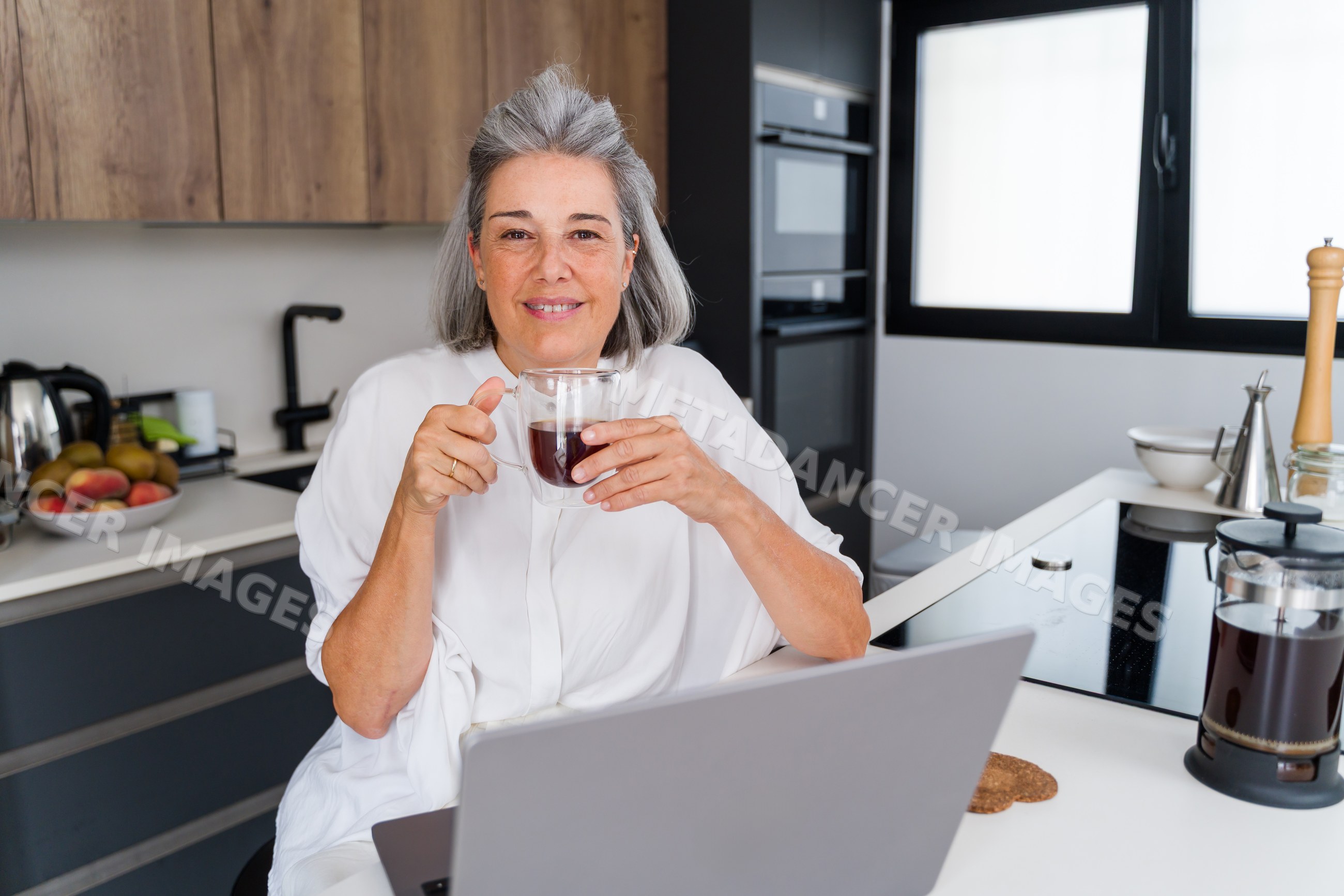 Middle aged white woman drinking coffee using laptop
