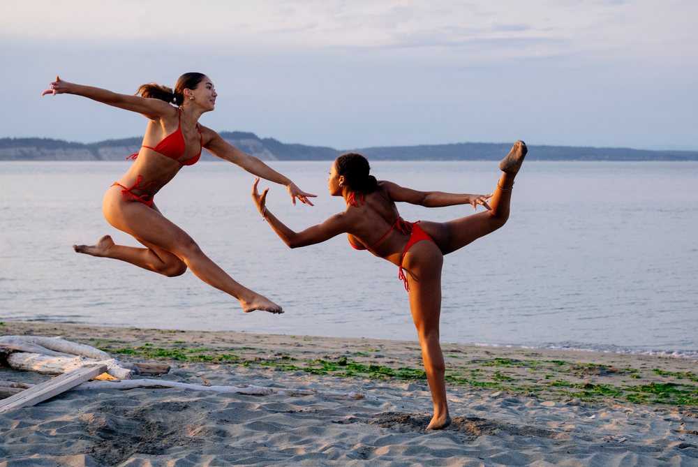 Two women practicing partner acrobatics yoga on a beach in wa USA